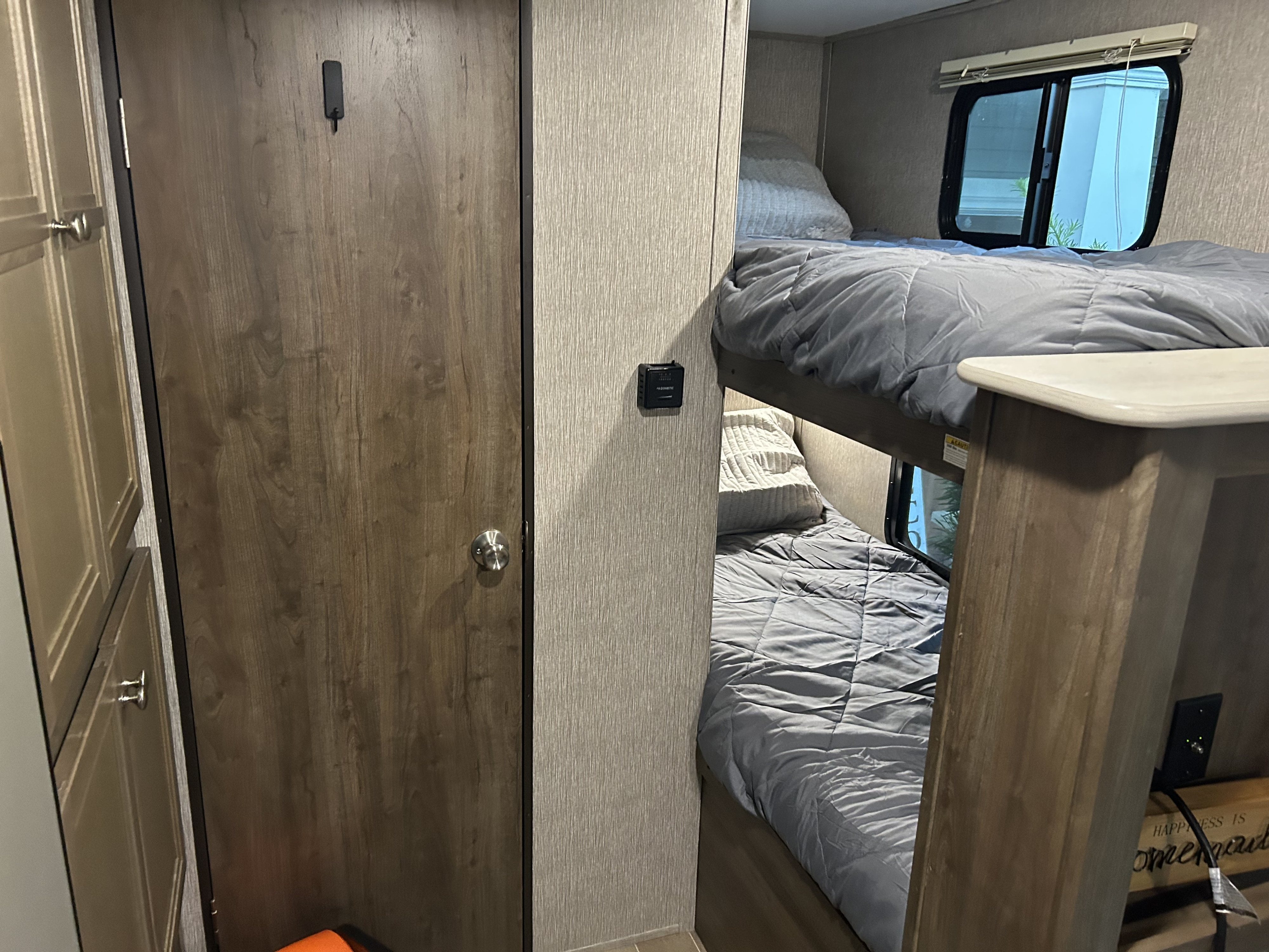 Cozy RV rental interior featuring twin bunk beds with gray bedding, a wooden door, and a thermostat. Perfect for family adventures.. Dutchmen Coleman Light LX 2020