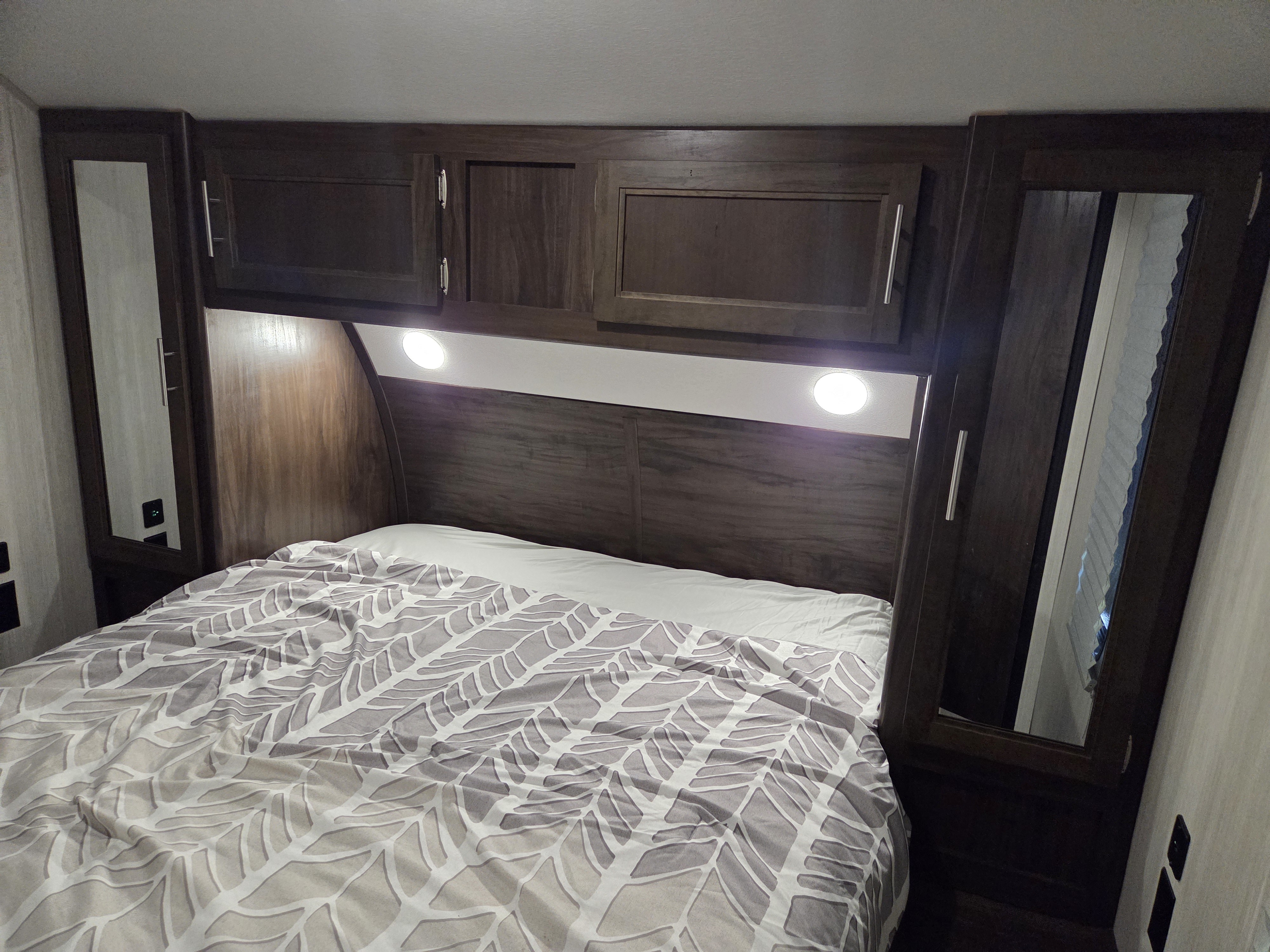 Cozy RV rental bedroom with a patterned bed, dark wood cabinets, bright reading lights, and ample storage.. Forest River Cherokee 2020