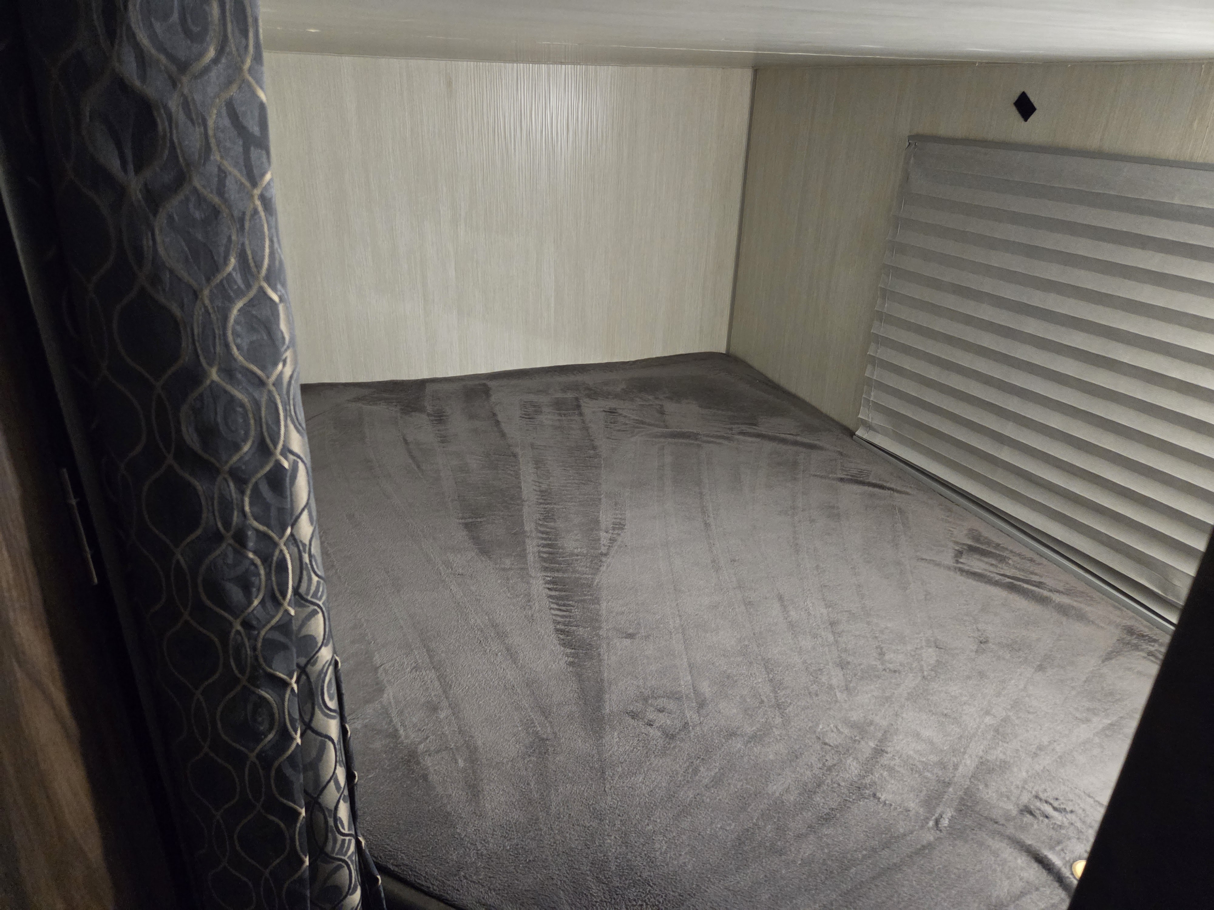 RV rental interior: A compact sleeping nook with a plush gray bed, patterned curtain, and closed window blinds.. Forest River Cherokee 2020