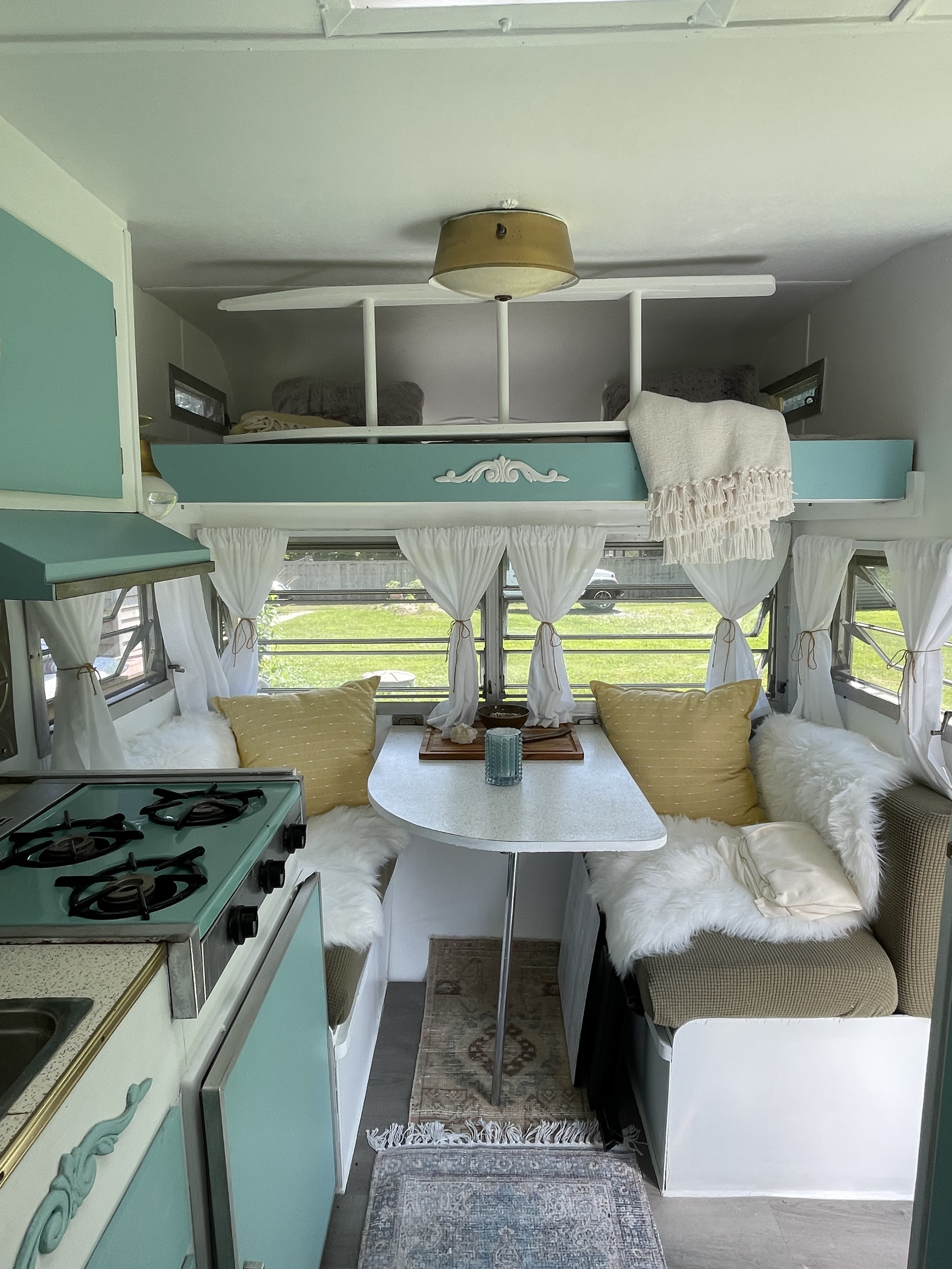 Cozy RV rental interior with retro teal accents, dining area, and a loft bed. Perfect for your next adventure!. Yellowstone Yellowstone 1965