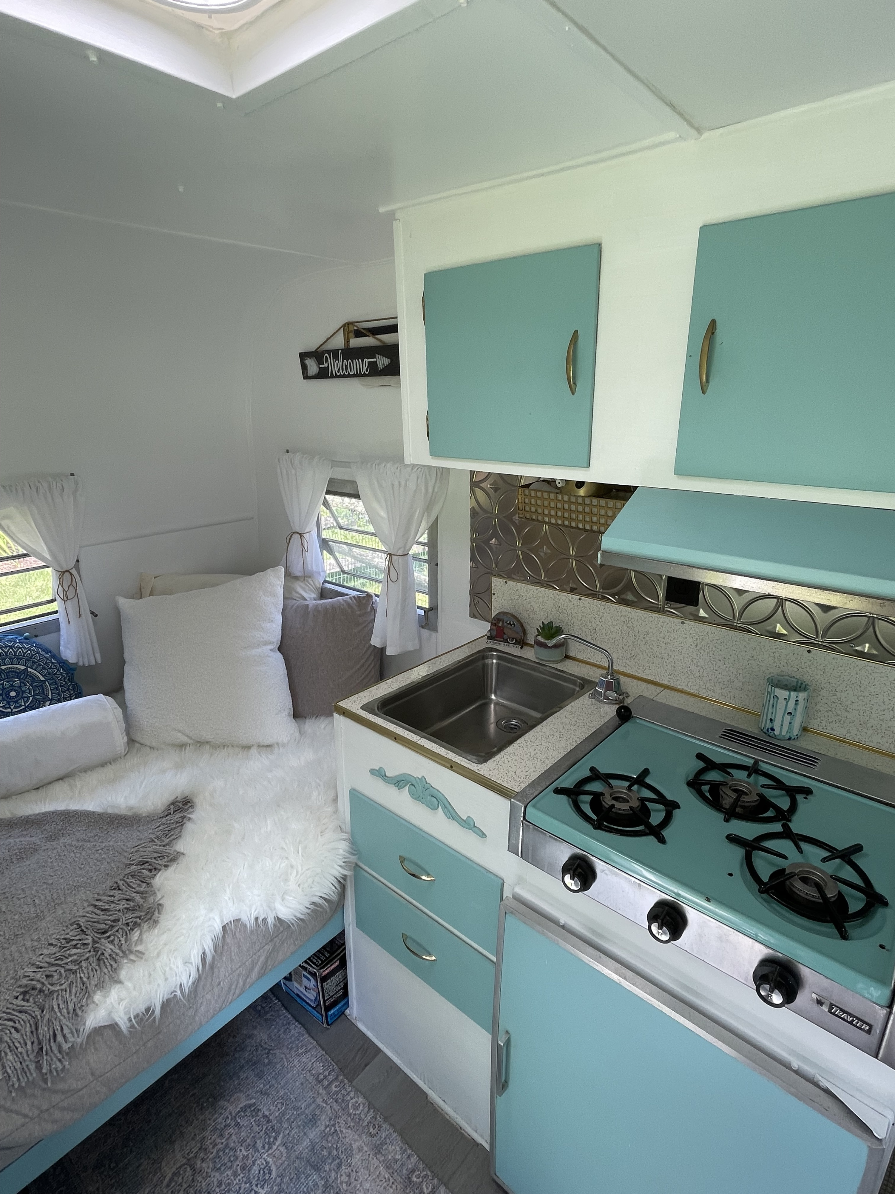 Inside this retro rv rental: a stylish light blue kitchenette, complete with a stove and sink, and a comfortable bed.. Yellowstone Yellowstone 1965