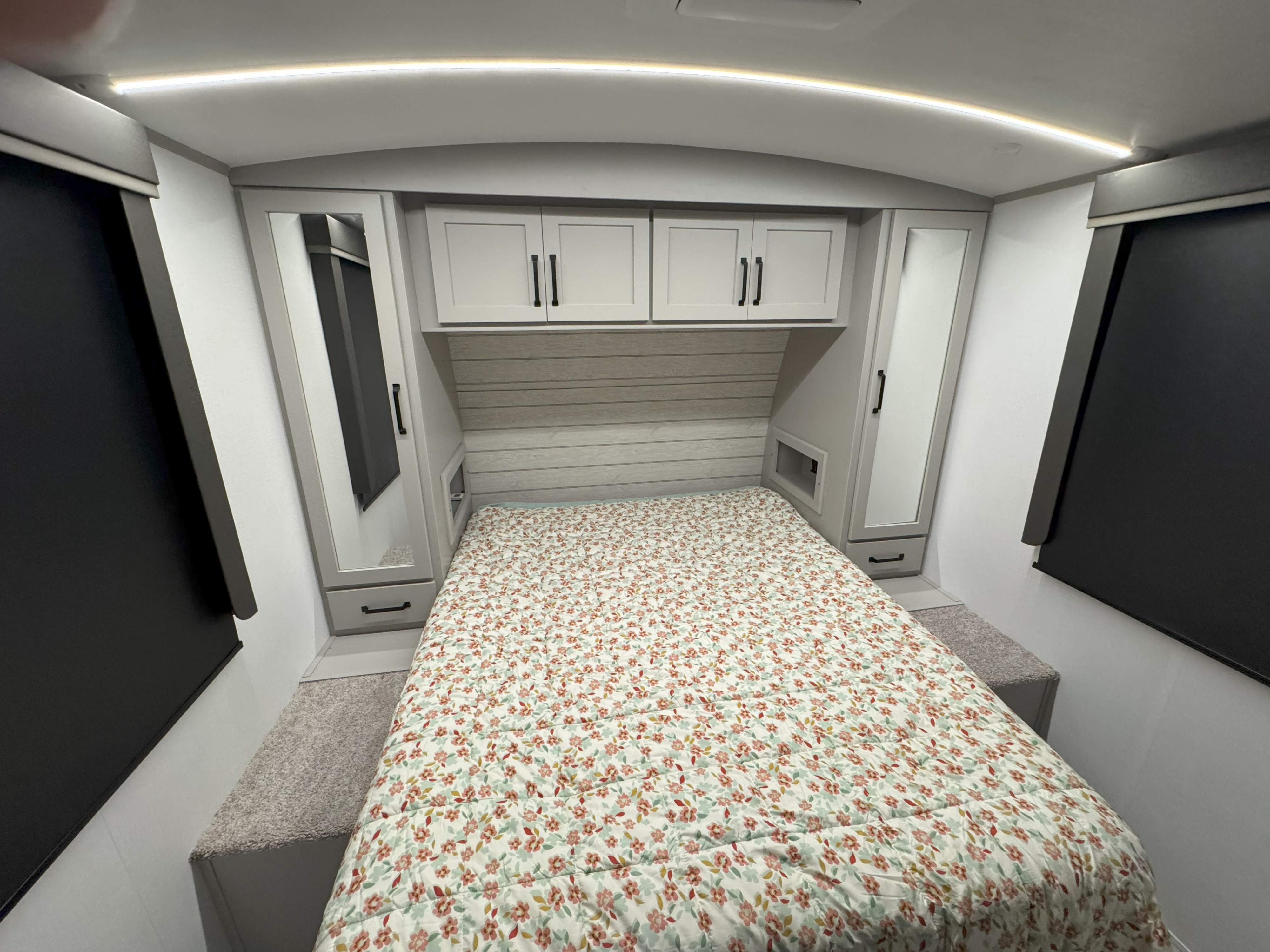 Cozy RV rental bedroom with floral bedding, overhead storage, mirrored wardrobes, and blackout blinds.. Keystone Outback 291BH 2025
