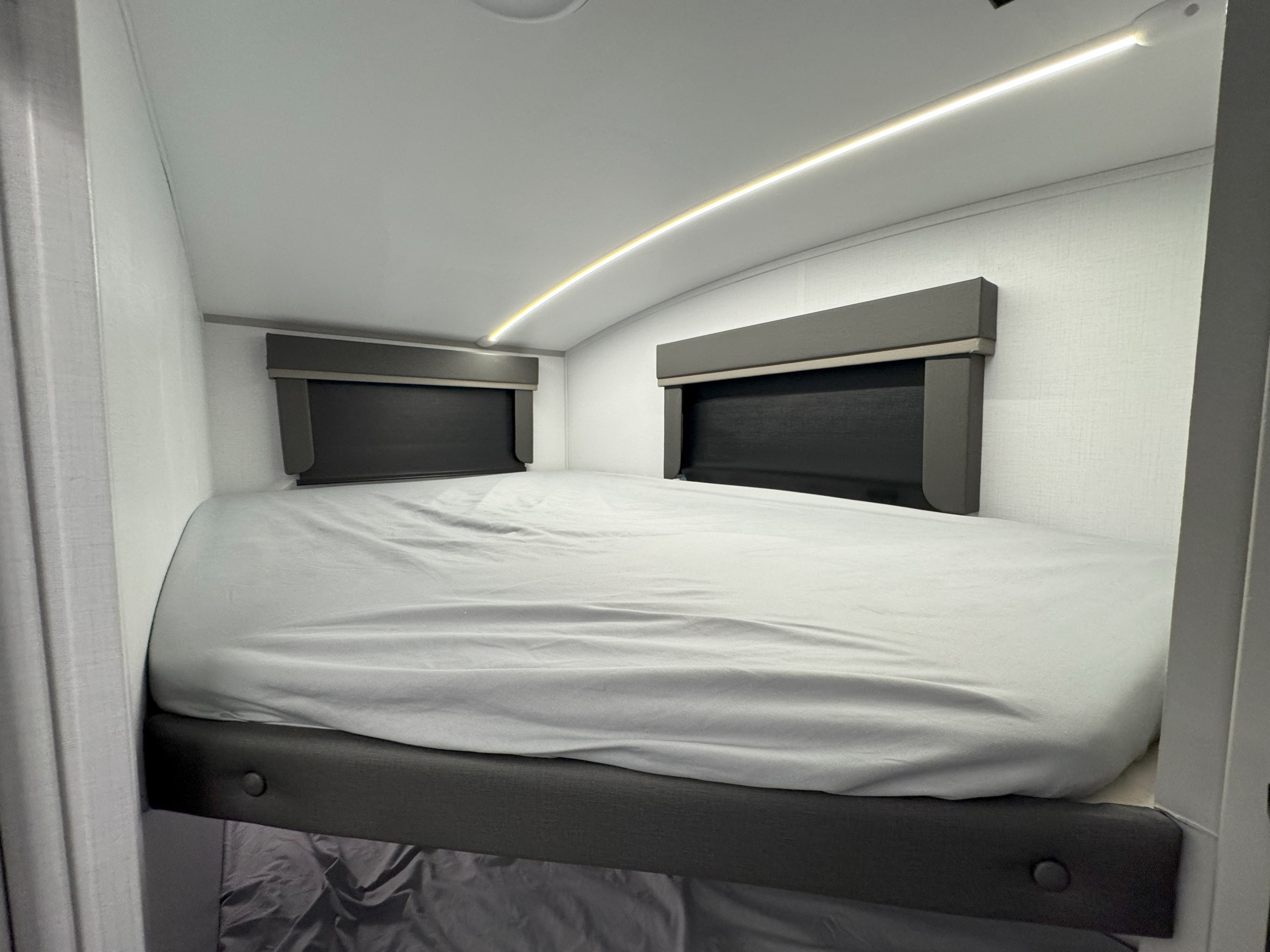 Modern RV rental bunk bed with clean gray sheets, two windows, and curved LED lighting on a light-colored wall.. Keystone Outback 291BH 2025