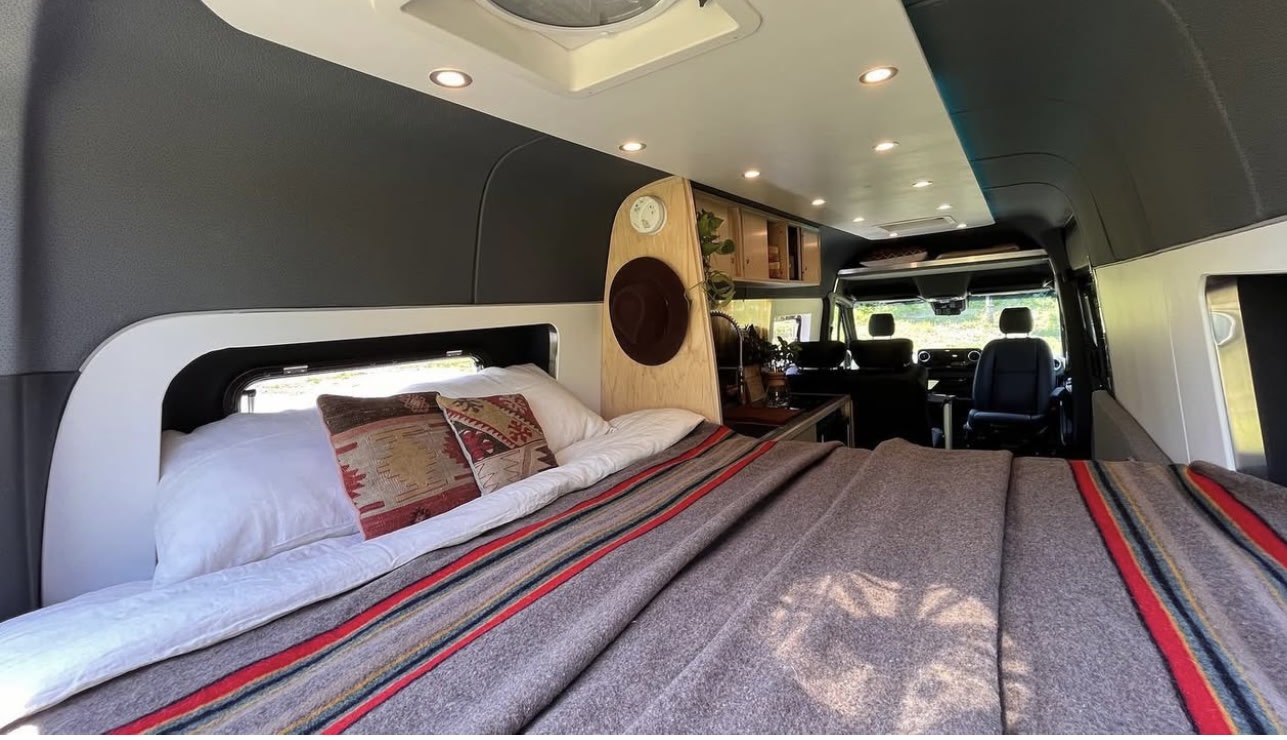 Cozy RV rental interior with a comfy bed, pillows, and view into the camper van's front seats.. Mercedes Sprinter 2022