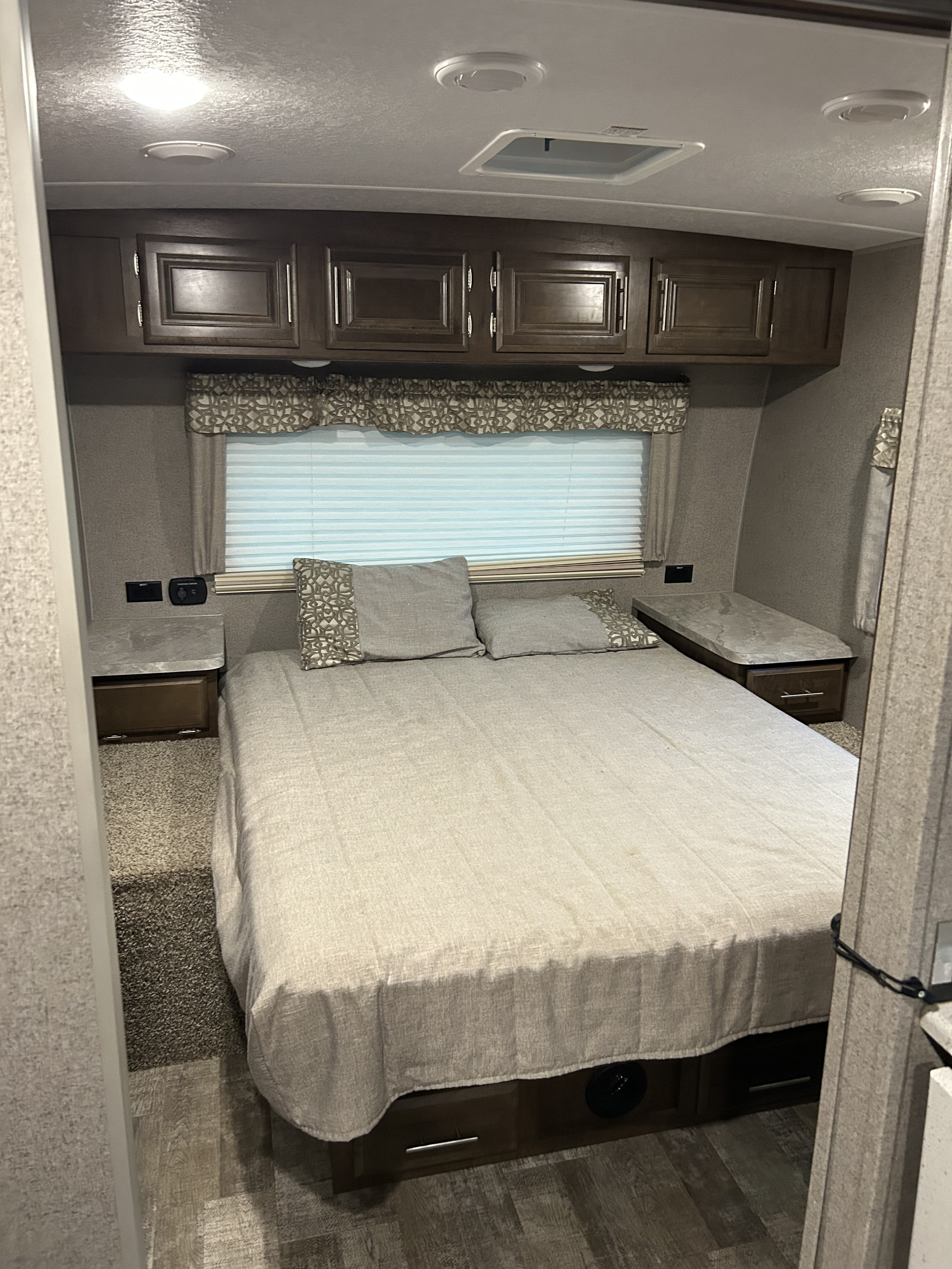 Cozy RV rental bedroom features a bed, overhead cabinets, window with blinds, and bedside tables.. Forest River Rockwood Ultra Lite 2022
