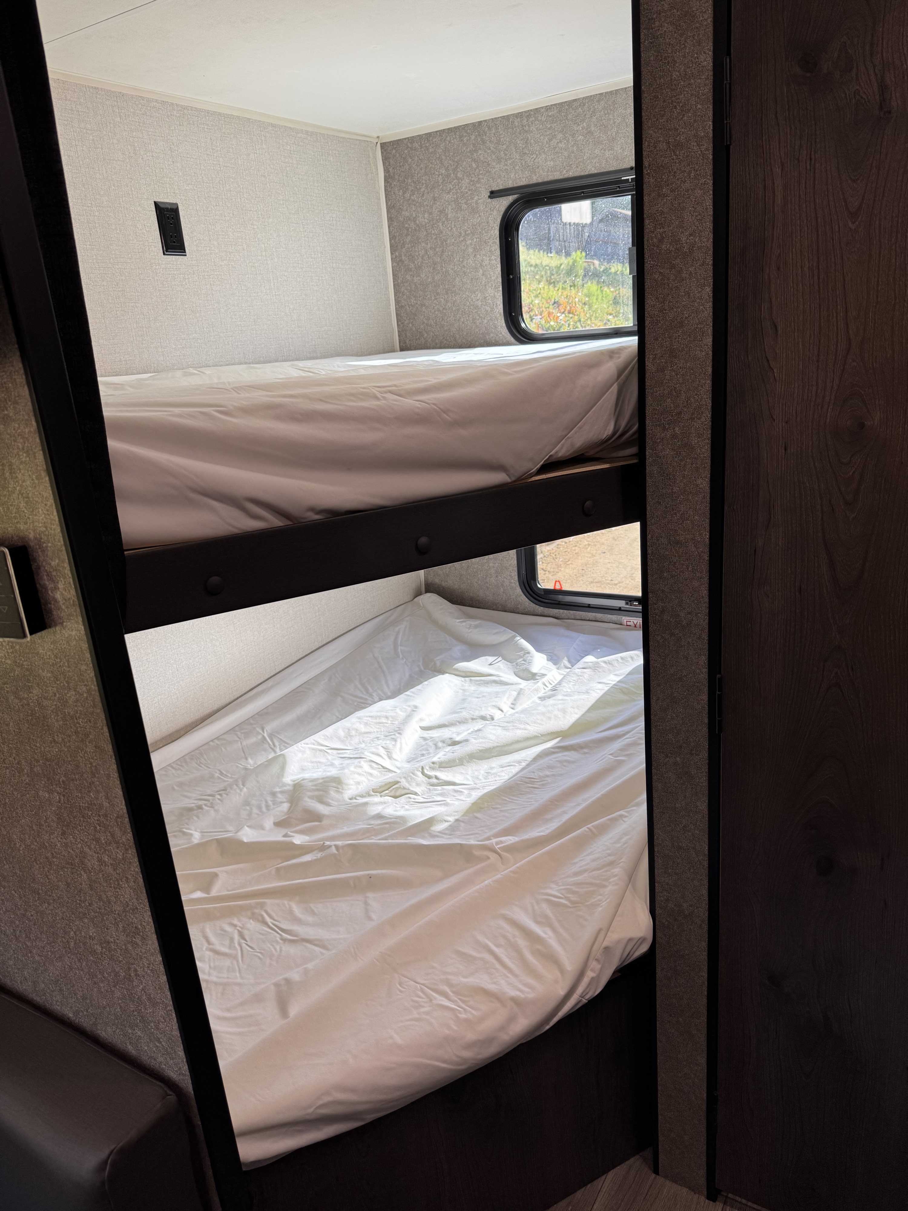 Inside an rv rental: stacked bunk beds with white linens, windows, and an outlet, offering compact sleeping space.. Starcraft Autumn Ridge 2021