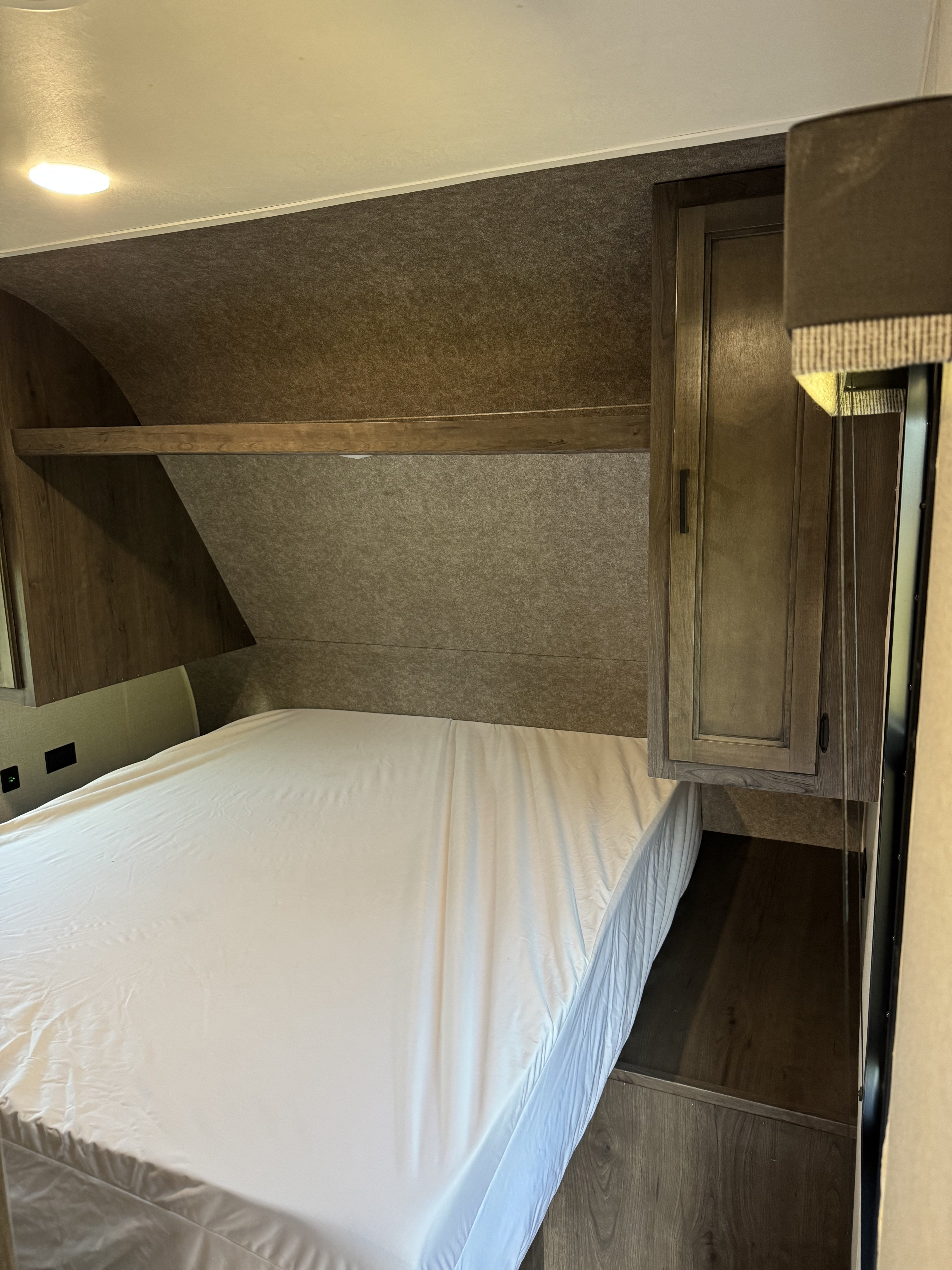 RV rental bedroom interior featuring a white-sheeted bed, overhead storage shelf, and cabinet, for comfortable living.. Starcraft Autumn Ridge 2021