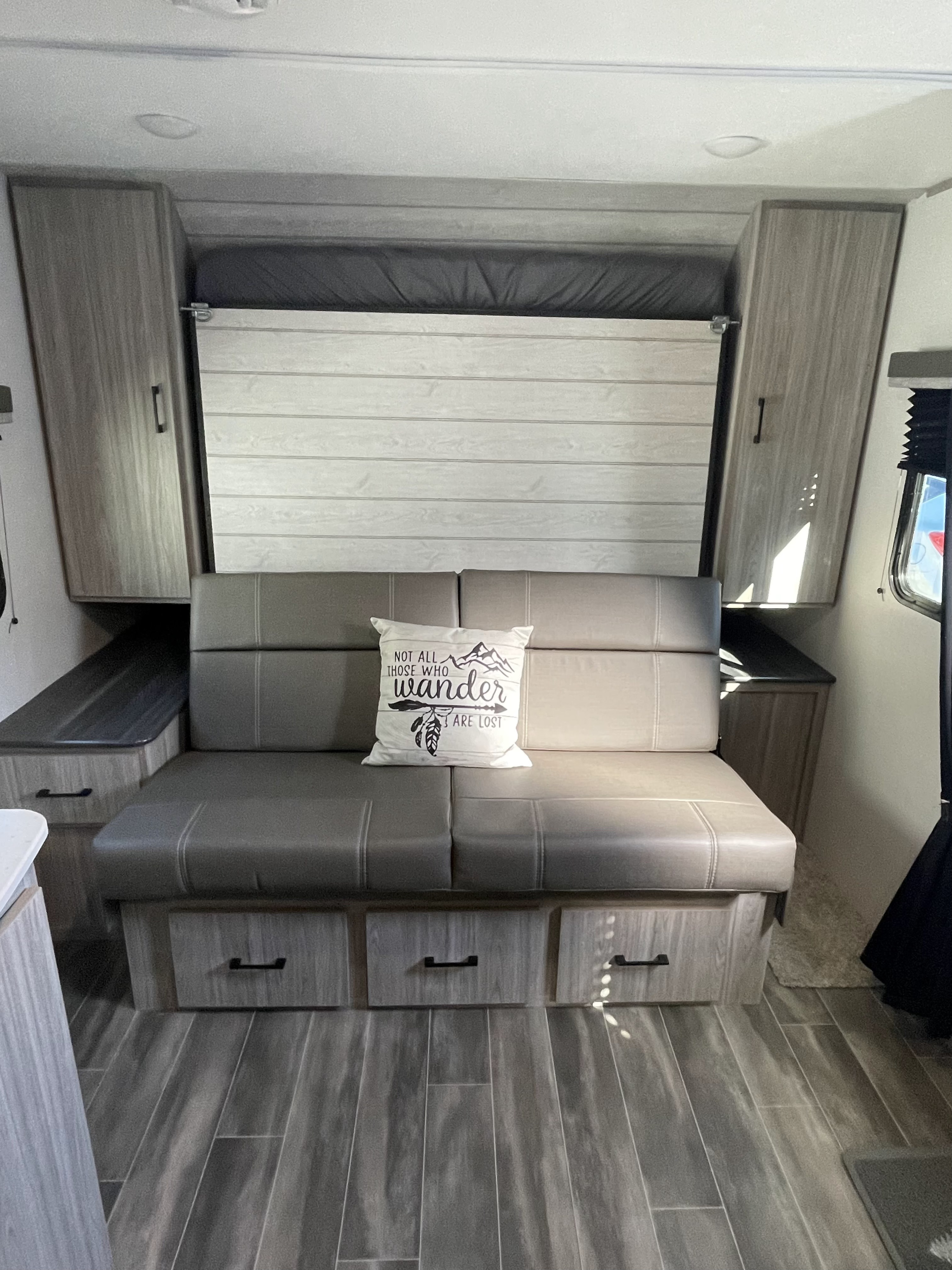 Cozy RV rental interior showcasing a gray sofa, a stowed bed above, and wood-look storage cabinets. Ideal for travel adventures.. Keystone RV Passport SL 2022