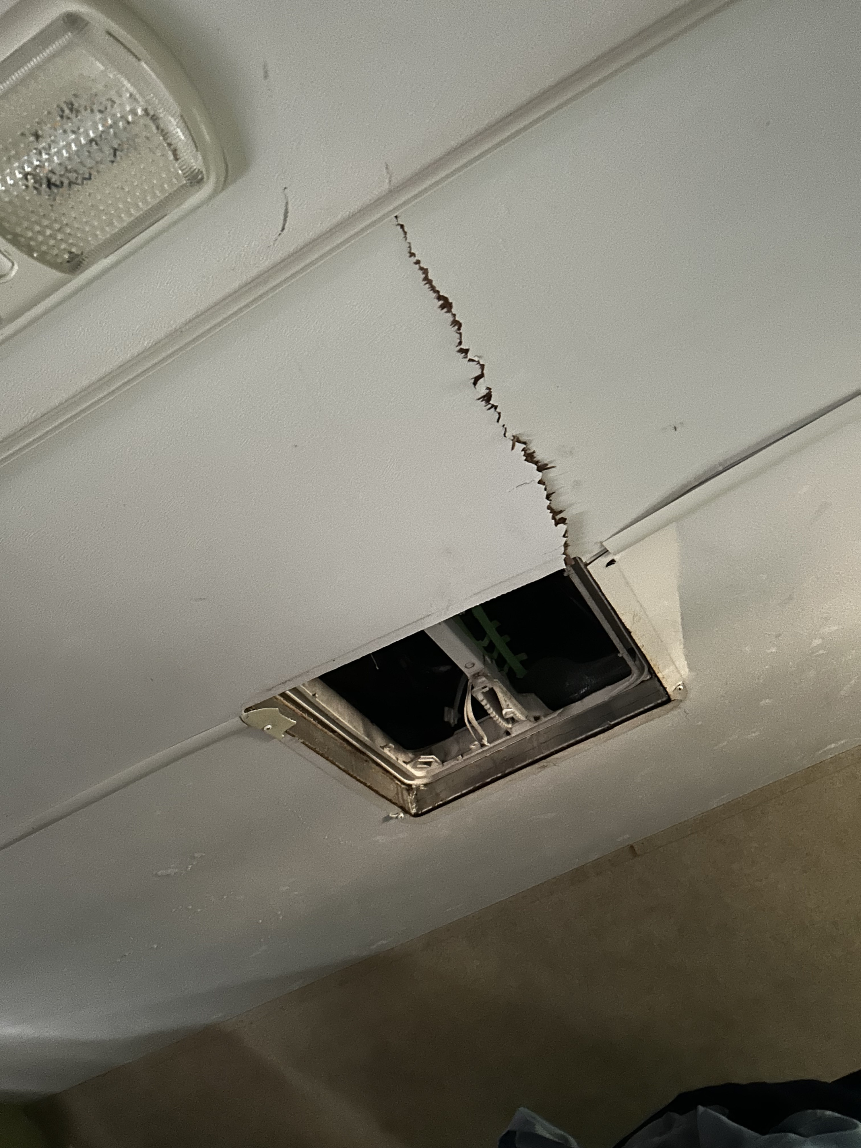 RV rental ceiling damage: a jagged tear near an open vent exposes interior wiring. A light fixture is visible.. Thor Majestic 2015