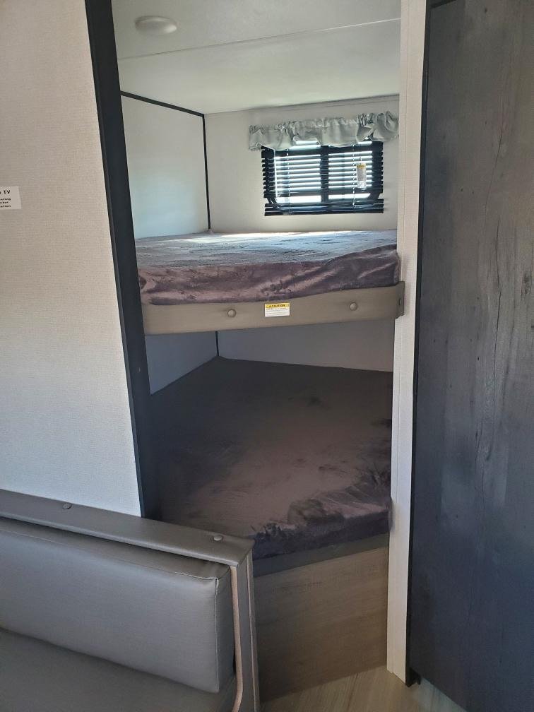 Inside an RV rental: a bright interior shows cozy bunk beds, a window, and a seating area. Perfect for family camping.. Keystone RV Hideout 2021