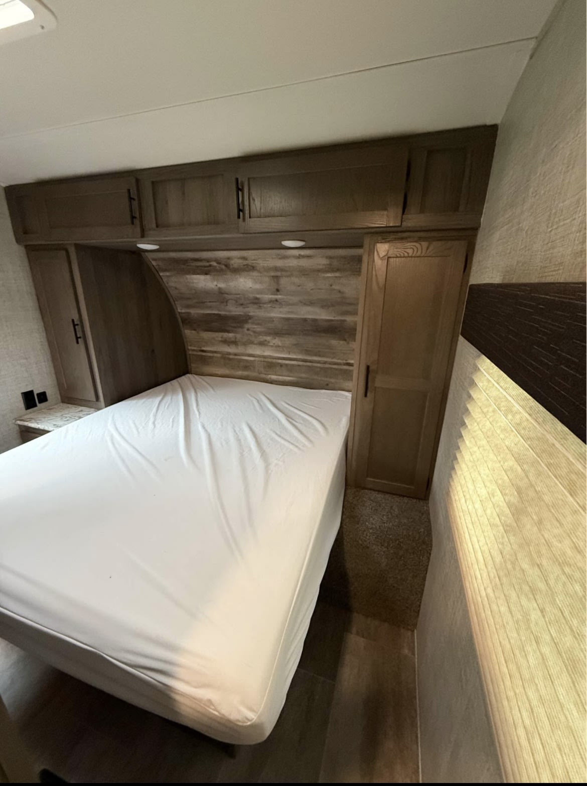 Compact RV rental bedroom with a white-sheeted bed, overhead cabinets, and wooden accents.. Gulf Stream Kingsport Supreme 2020