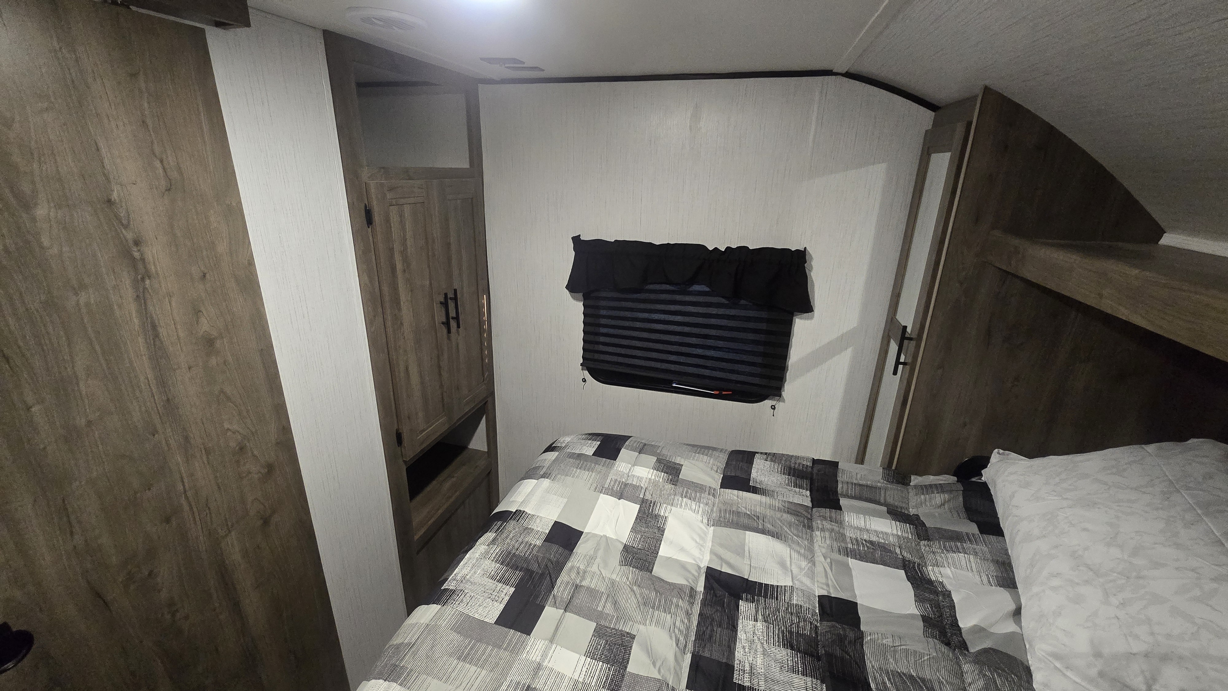 Cozy RV rental bedroom featuring a patterned bed, window with blinds, and wooden wardrobe, ideal for travel.. Heartland RVs Pioneer 2022