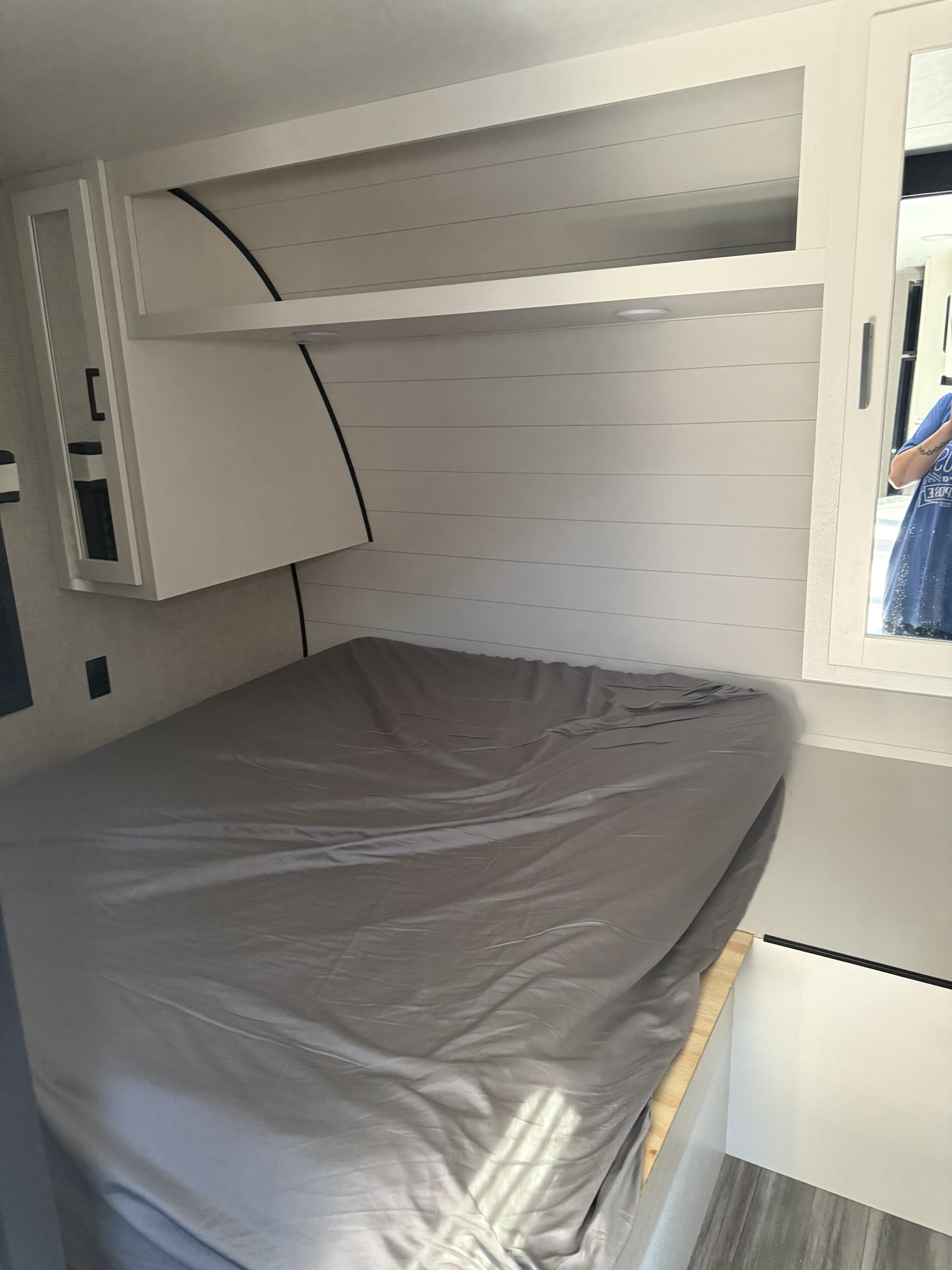 Explore this modern rv rental bedroom: gray bed, ample overhead storage, clean white shiplap walls, and mirror.. Jayco Jay Flight 2024