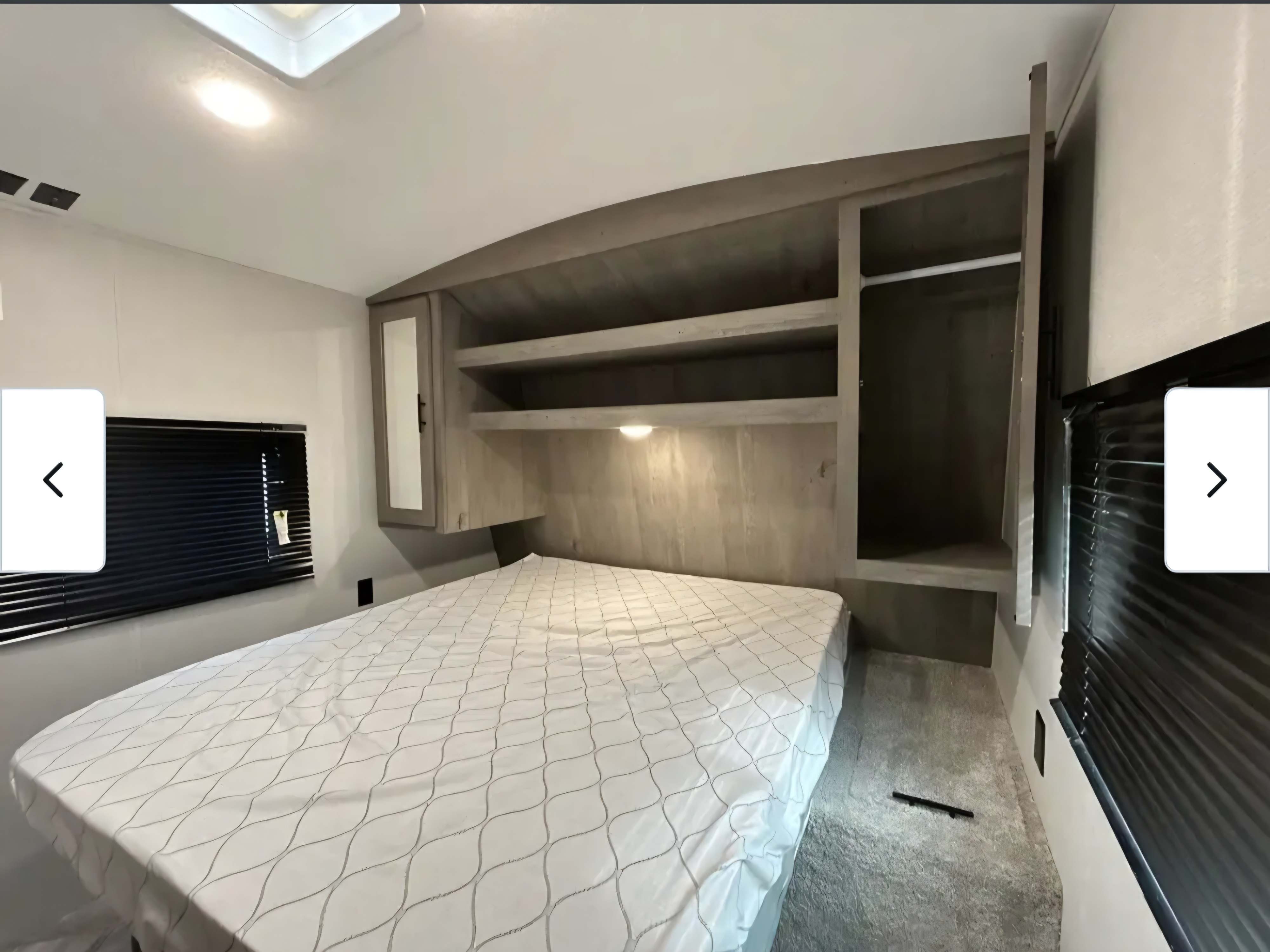 Cozy RV rental bedroom featuring a queen bed with patterned cover, overhead shelving, mirrored cabinet, and window blinds.. Keystone RV Springdale 2021