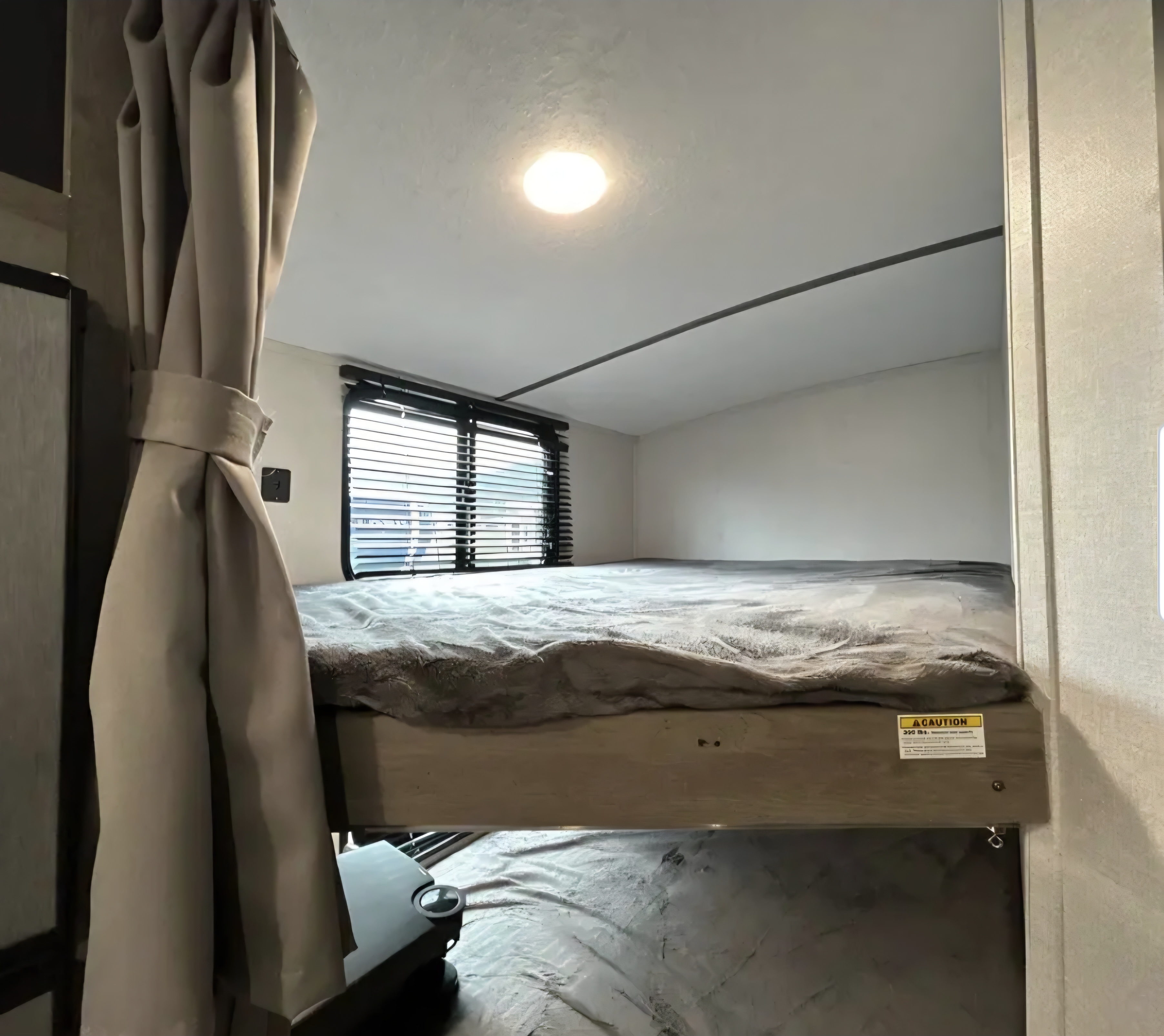 Interior of an RV rental featuring a comfortable bunk bed, window with blinds, and tie-back curtain. Overhead light visible.. Keystone RV Springdale 2021