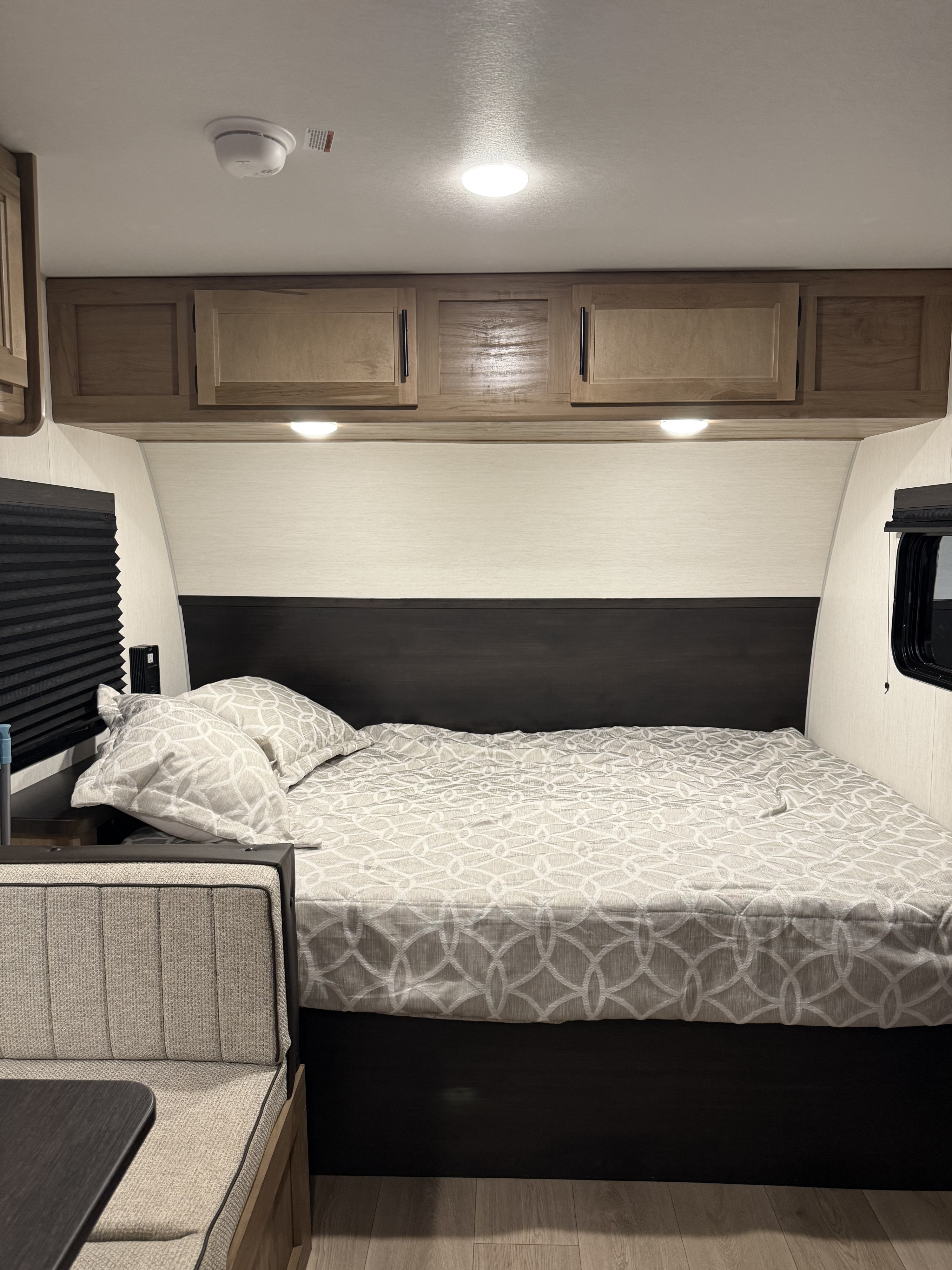 Inside an RV rental: a cozy bedroom with light patterned bedding, dark headboard, and wood-look flooring.. Forest River Cherokee 16BHS 2025