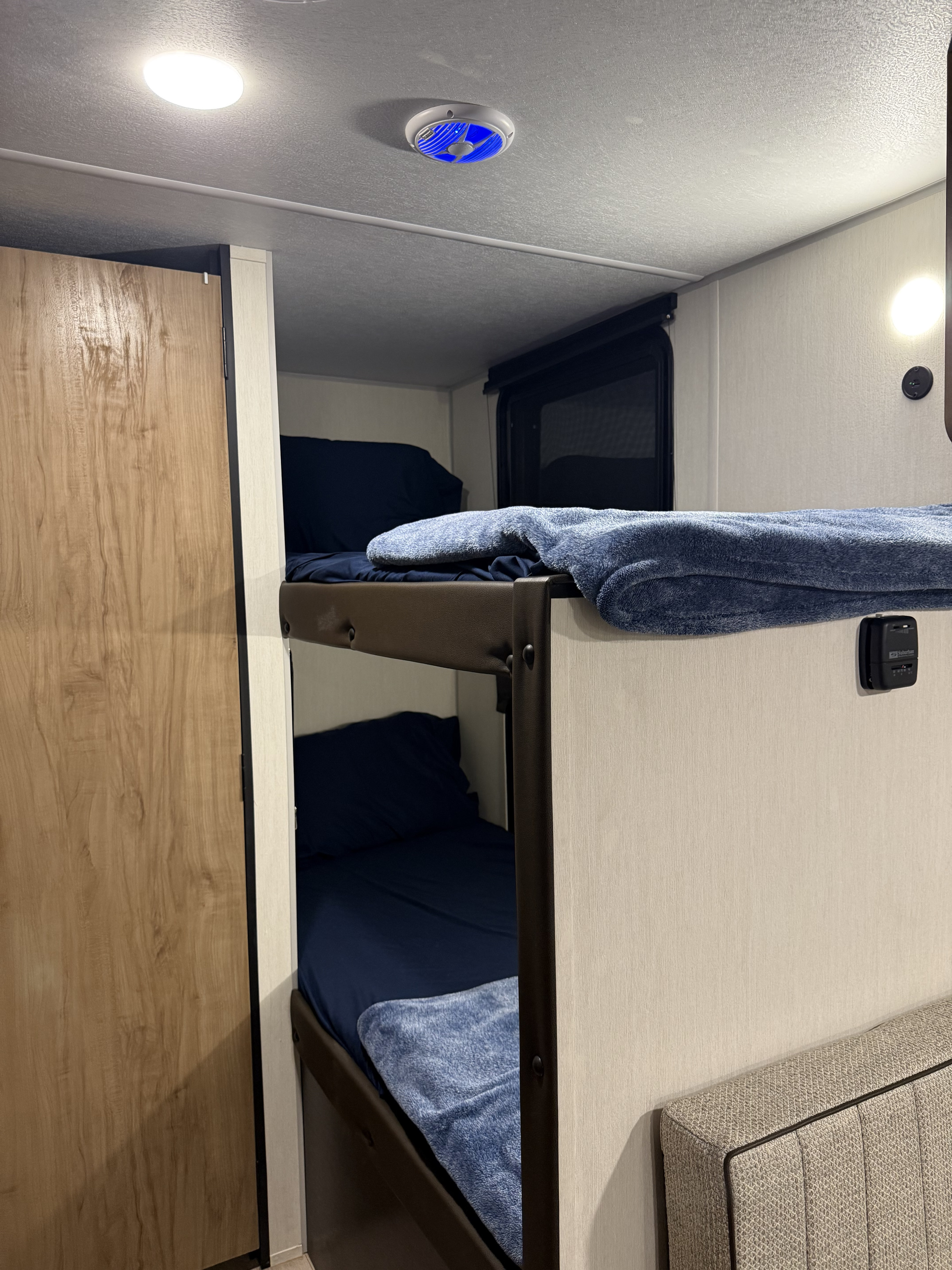 Cozy RV rental bunk beds with blue bedding, ceiling light, & blue fan. Perfect for travel.. Forest River Cherokee 16BHS 2025