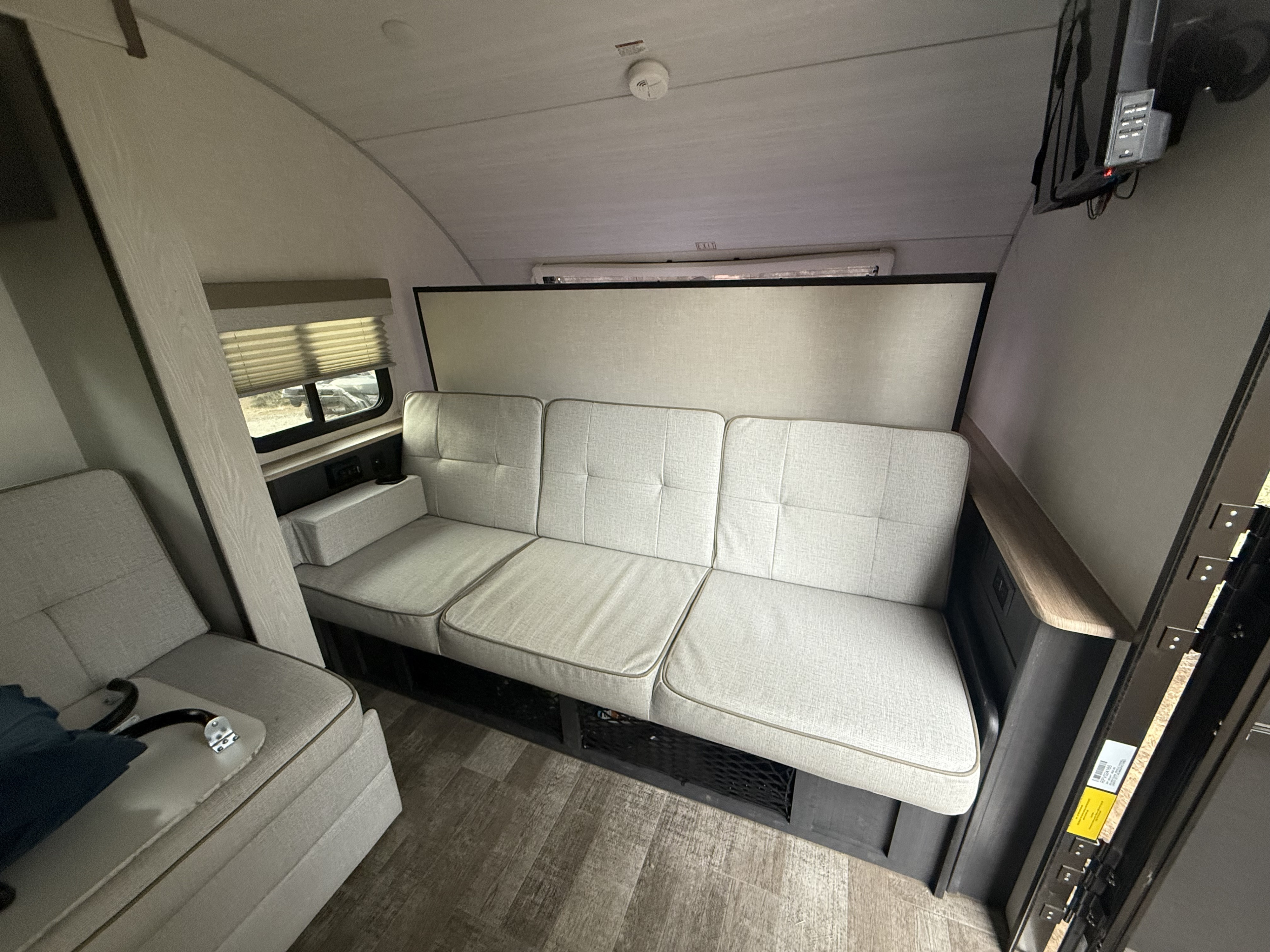 Modern RV rental interior with a versatile light gray sofa, window, TV, and wood-look flooring.. R-Pod R-Pod Trailer 2023