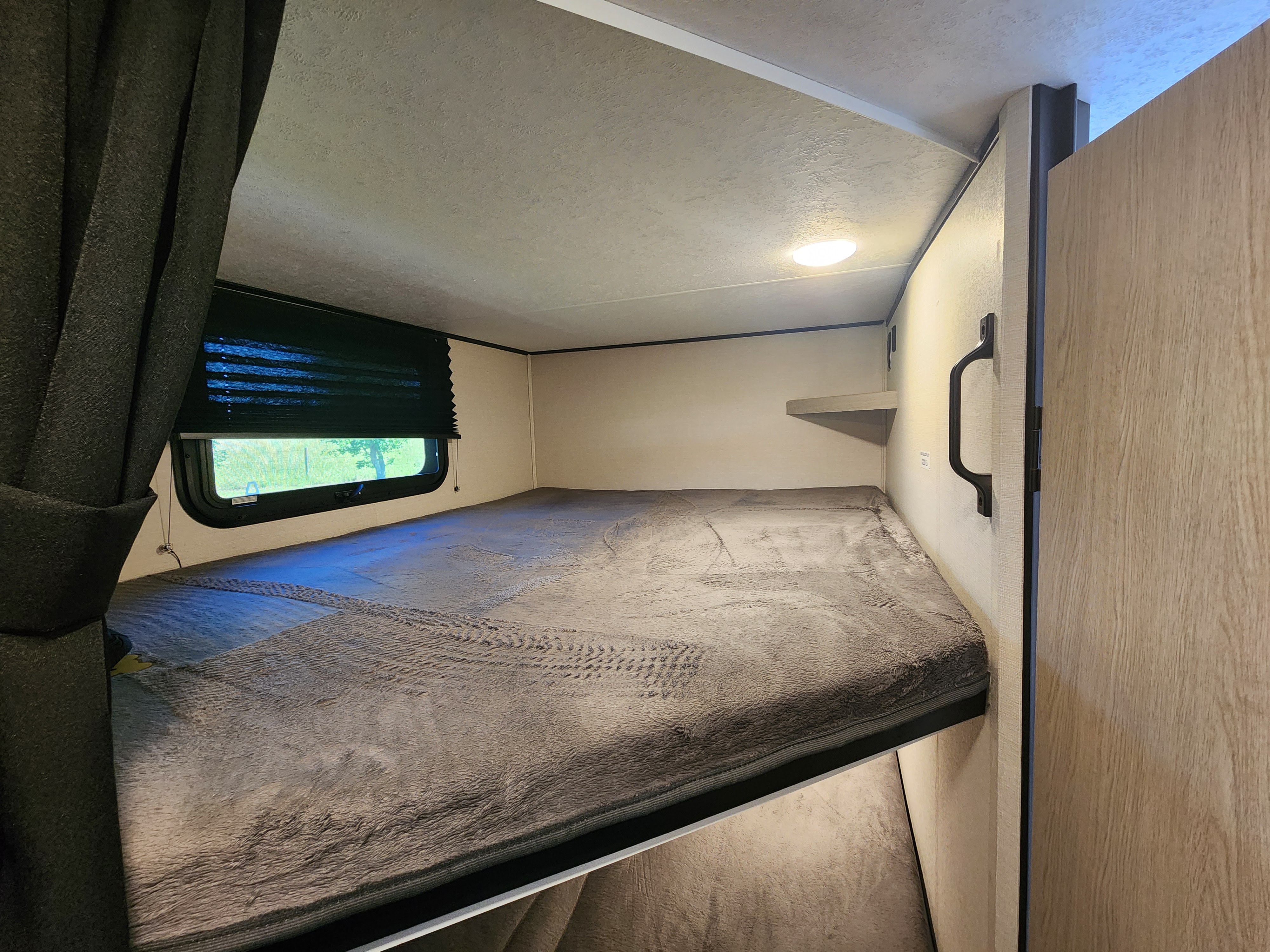 RV rental bunk bed with soft grey blanket, window, and overhead light. Ideal for comfortable travel.. Coachmen Apex 2021