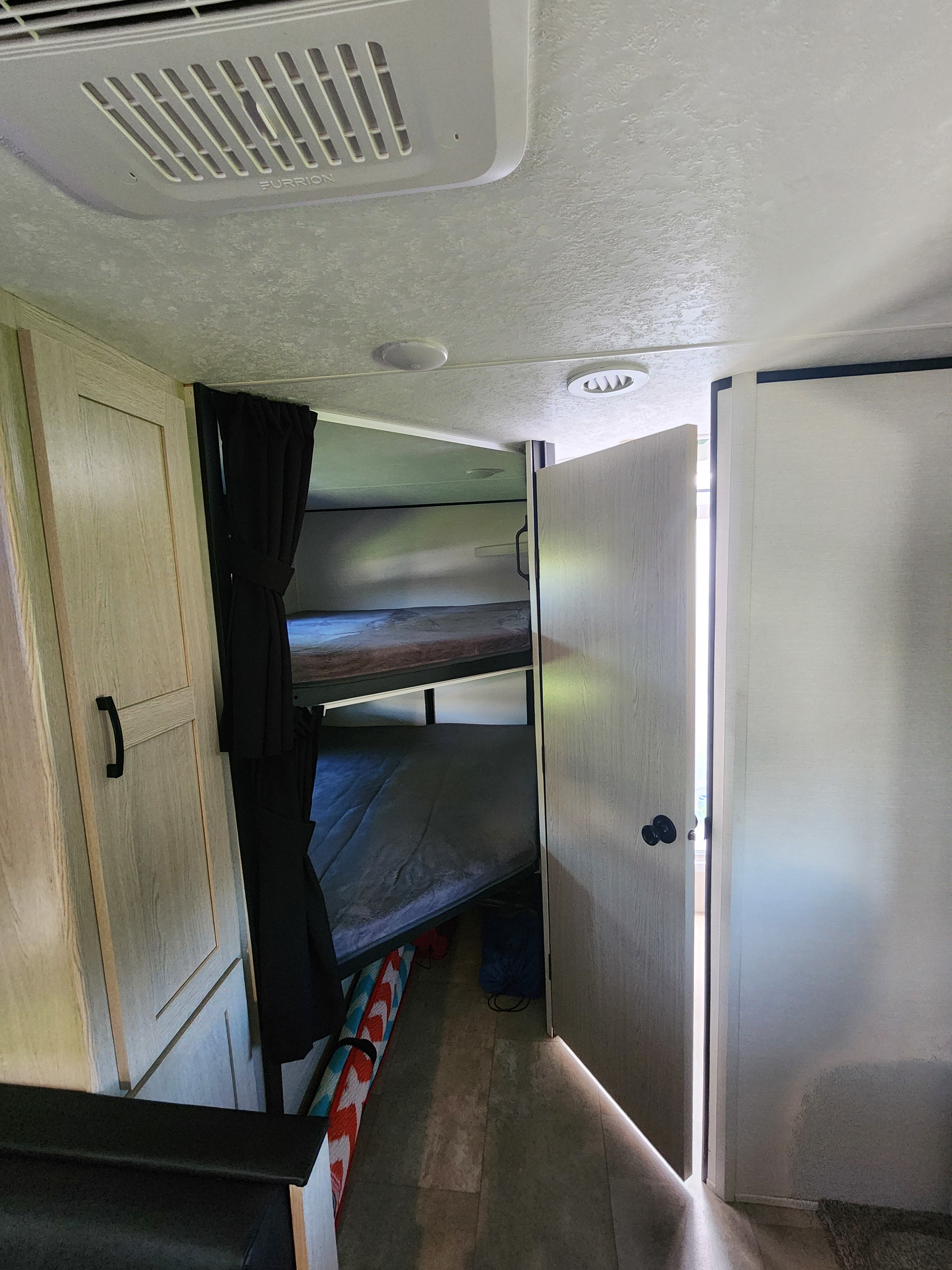 RV rental interior showing two bunk beds with privacy curtain, light wood cabinetry, and a Furrion AC unit overhead.. Coachmen Apex 2021