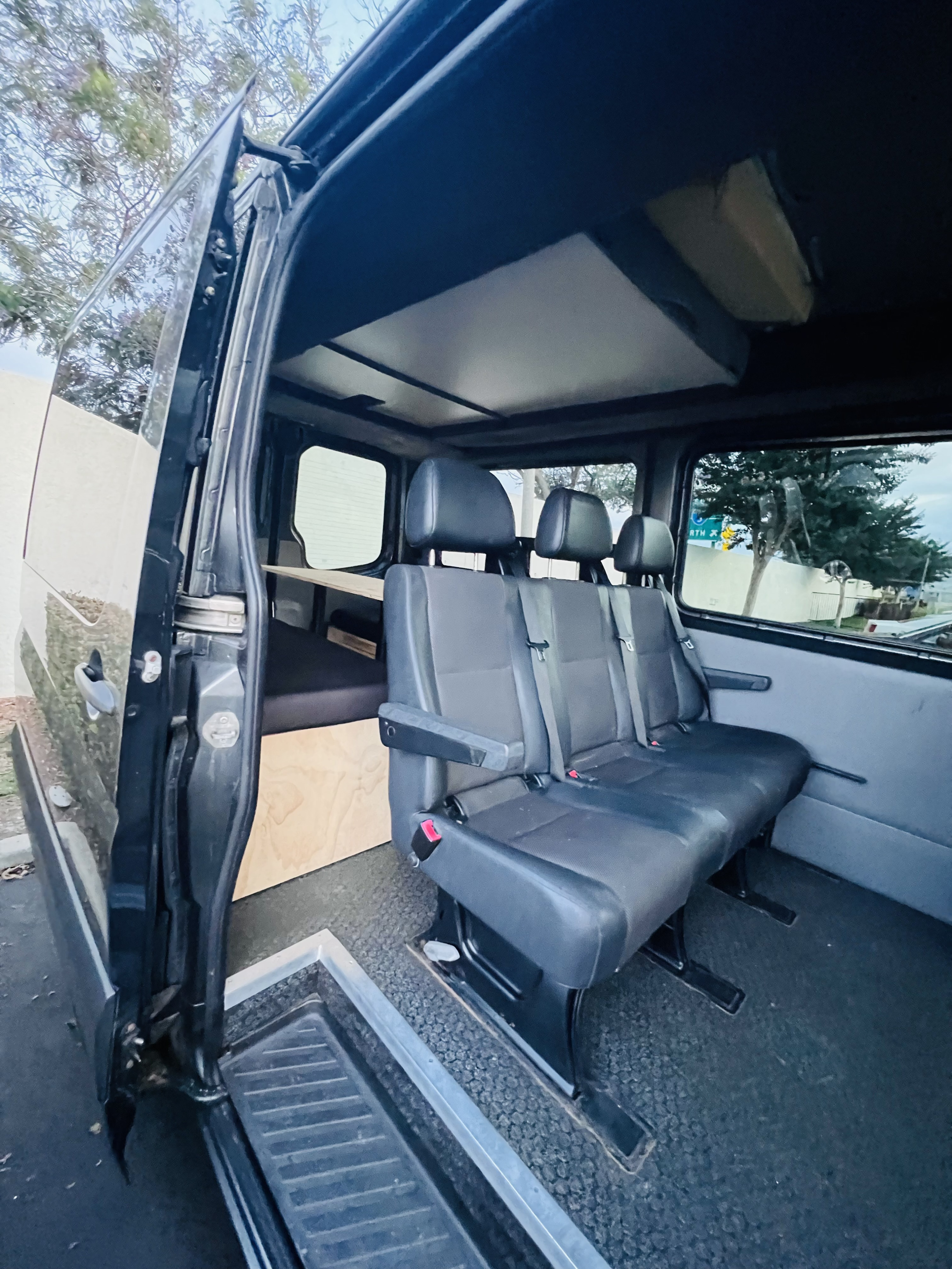Inside an RV rental van, featuring three passenger seats, a rear sleeping platform, and an open side door for easy access.. Mercedes-Benz Sprinter 2015