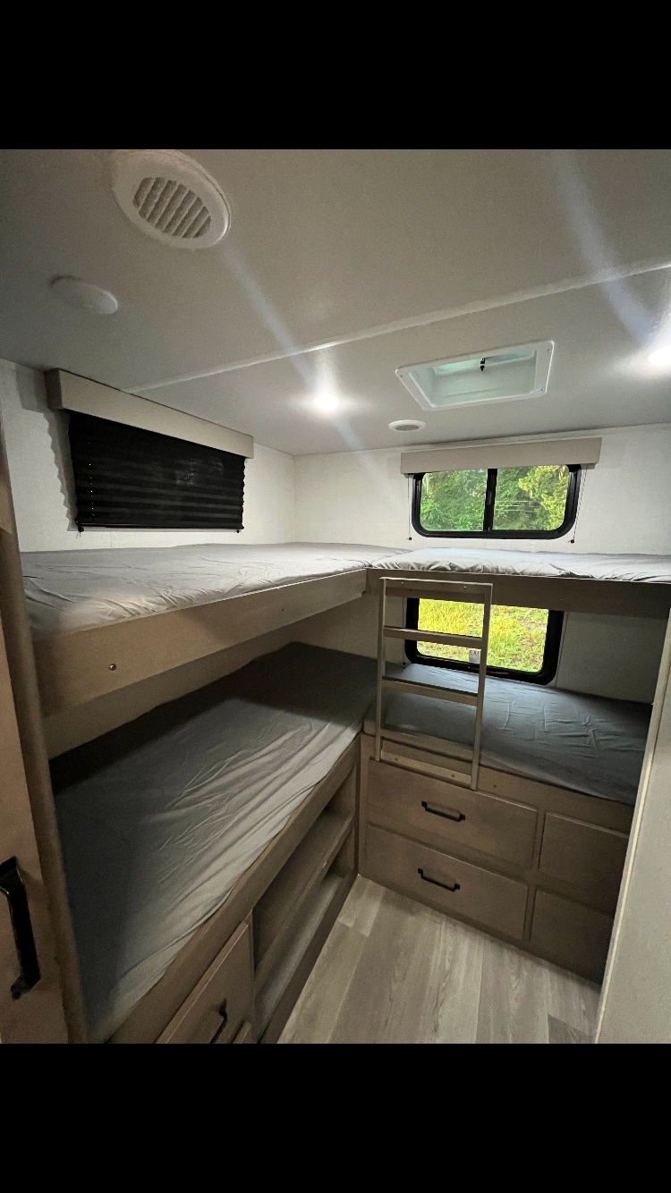 Cozy RV rental interior featuring L-shaped bunk beds with storage drawers, windows, and bright lighting. Perfect for family adventures!. Grand Design Transcend Xplor 2024