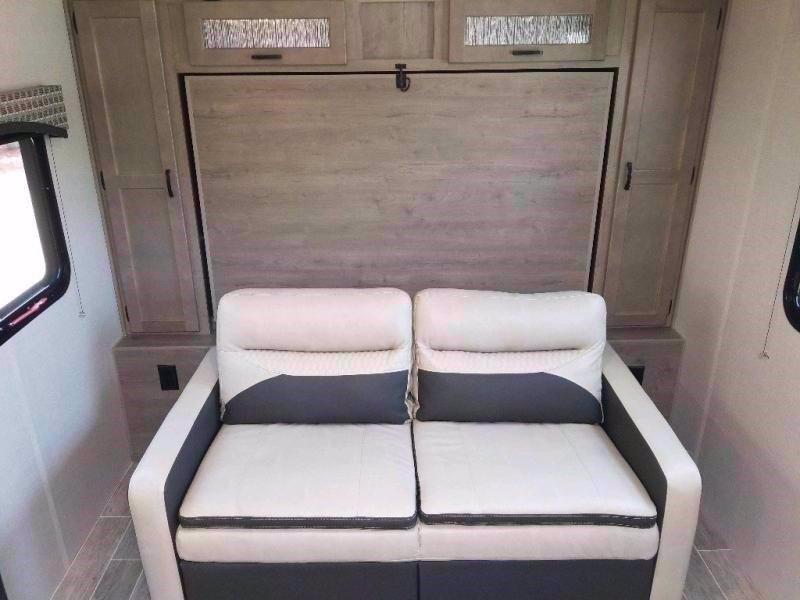 RV rental interior: Two-tone sofa below a discreet fold-down bed, flanked by storage cabinets.. Venture SonicX 2021