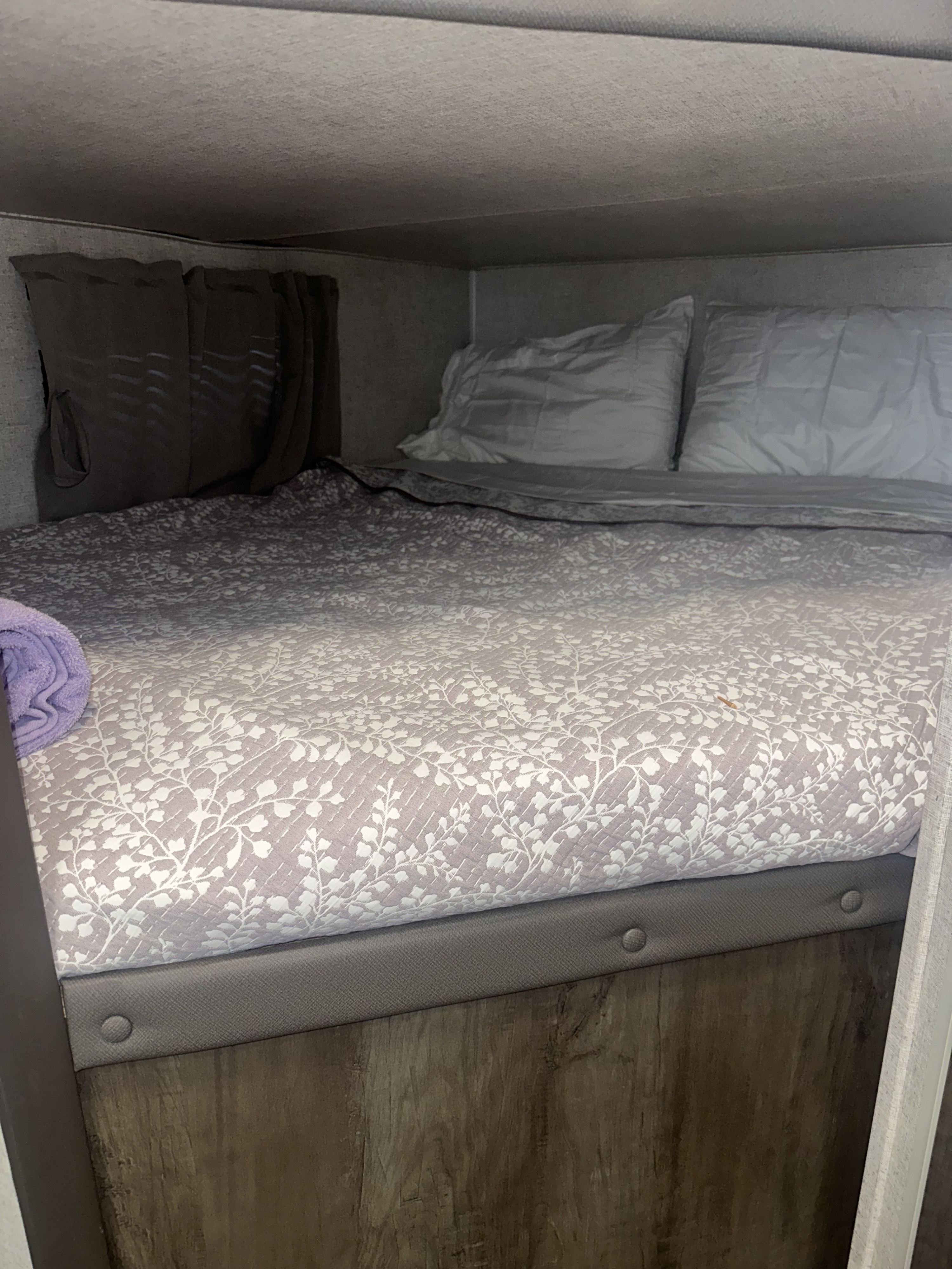 Cozy bunk bed inside an RV rental, featuring a light grey floral quilt, pillows, and privacy curtains.. Forest River Wildwood X-Lite 2022