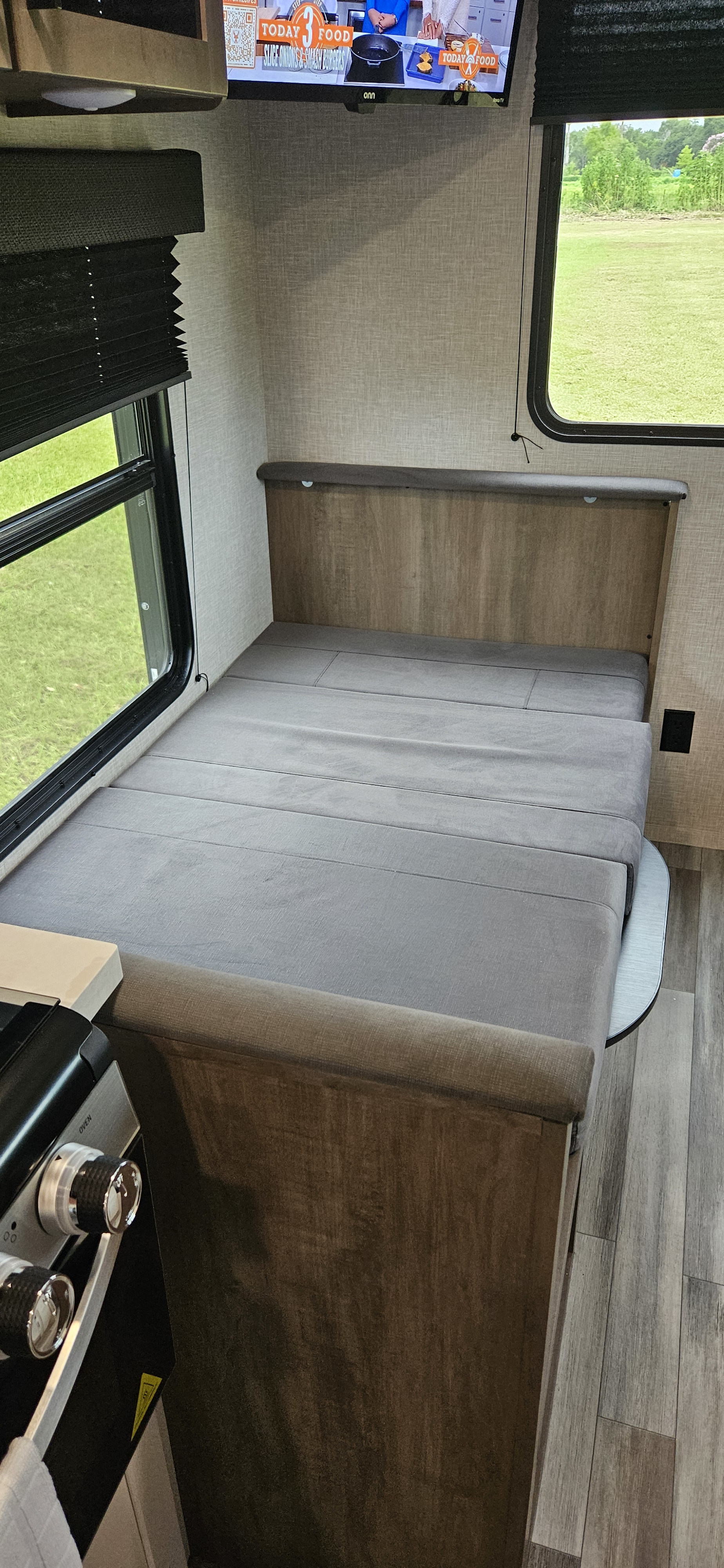 Cozy RV rental interior featuring a gray convertible bed, window with green views, wall-mounted TV, and a kitchen area.. Jayco Jay Flight SLX 210 QB 2025
