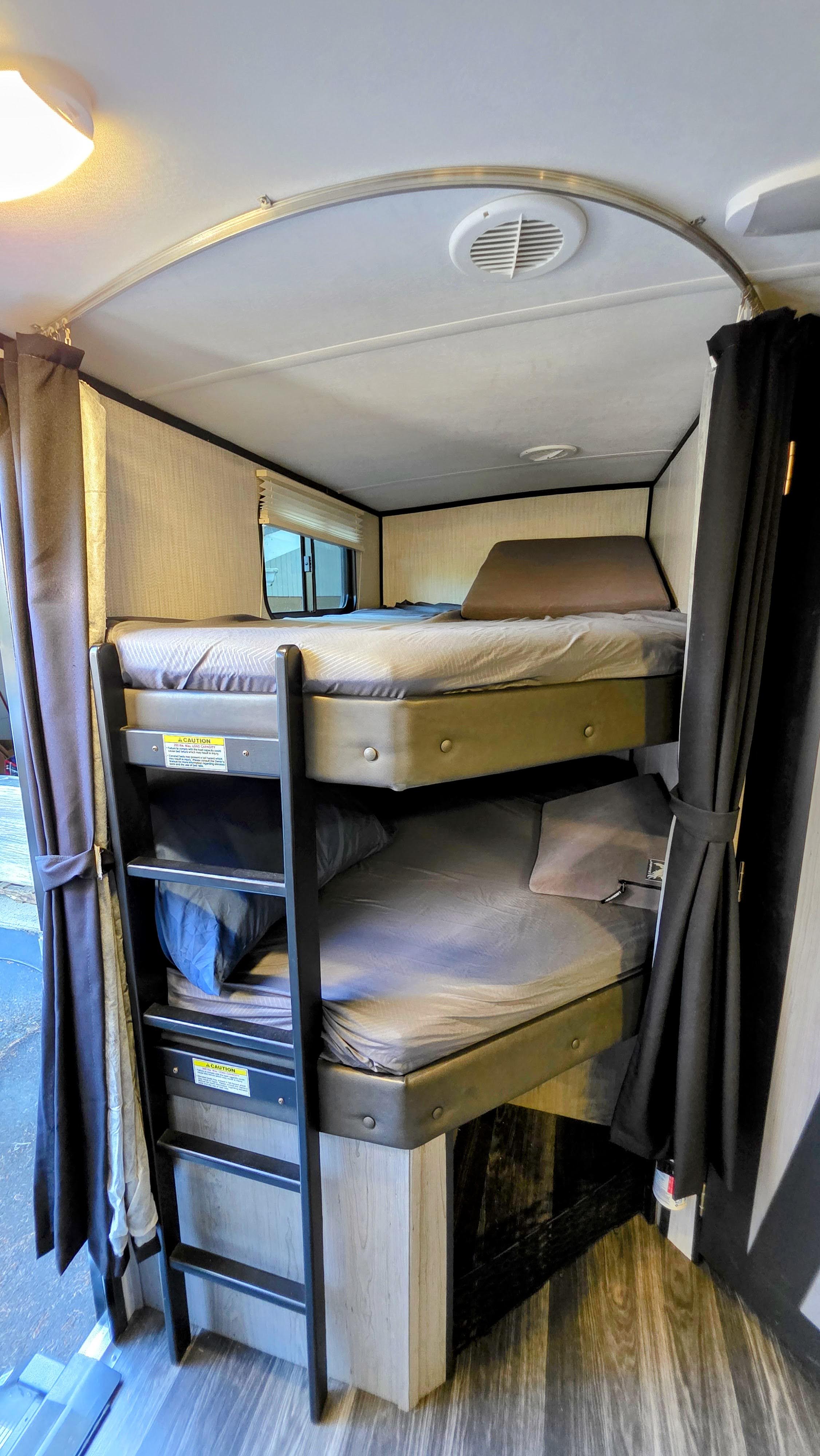 An RV rental interior featuring two comfortable bunk beds, a ladder for access, and privacy curtains on both sides.. Heartland RVs Mallard 2021