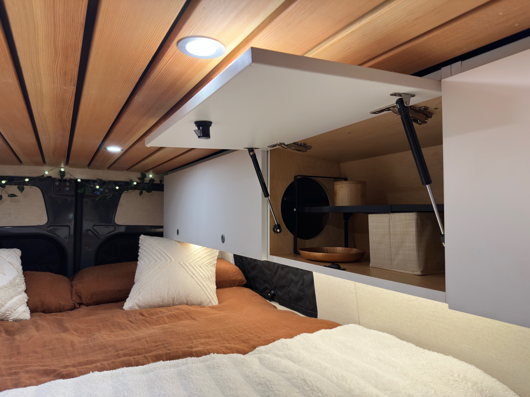 Cozy RV rental interior featuring a wooden ceiling, comfortable bed, and open overhead storage cabinets. Ideal for a campervan trip.. Mercedes-Benz Sprinter 2021