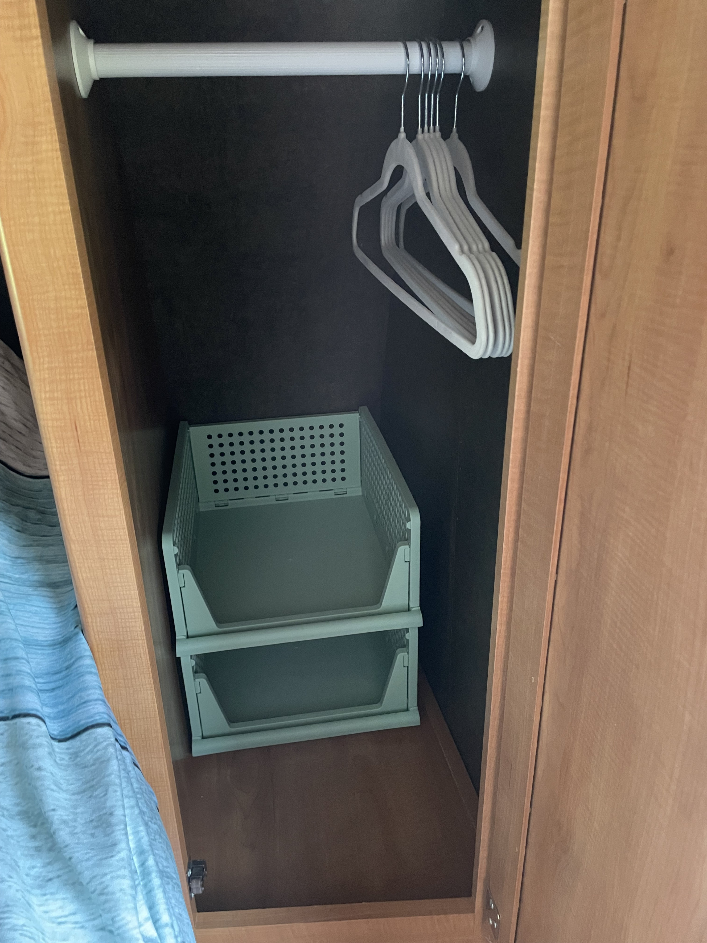 Inside an RV rental closet: a tension rod with white hangers above two stacked sage green storage bins within light wood cabinetry.. Forest River Shasta Flyte 2015