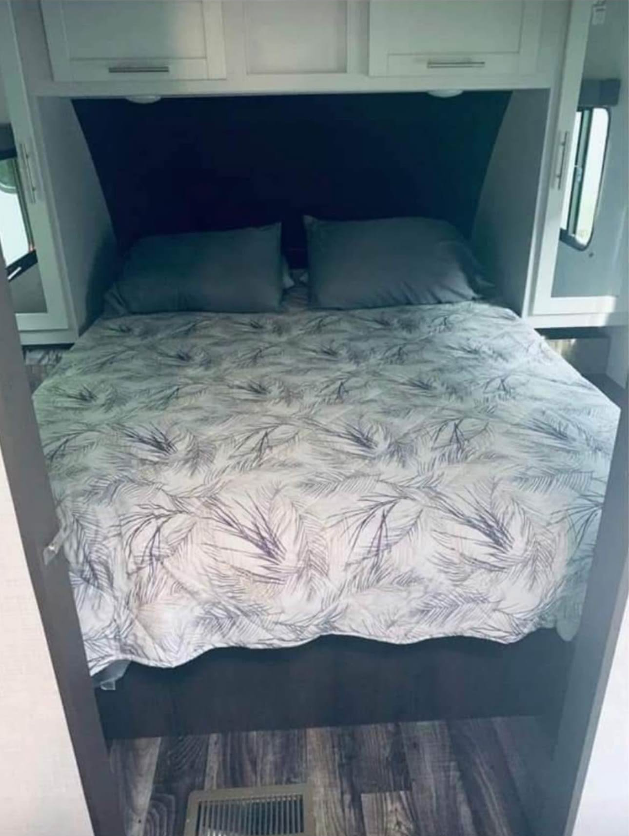 Cozy RV rental bedroom. Features a comfortable bed with leaf-patterned duvet, pillows, overhead cabinets, and side windows.. Keystone RV Bullet Ultra Lite 2020