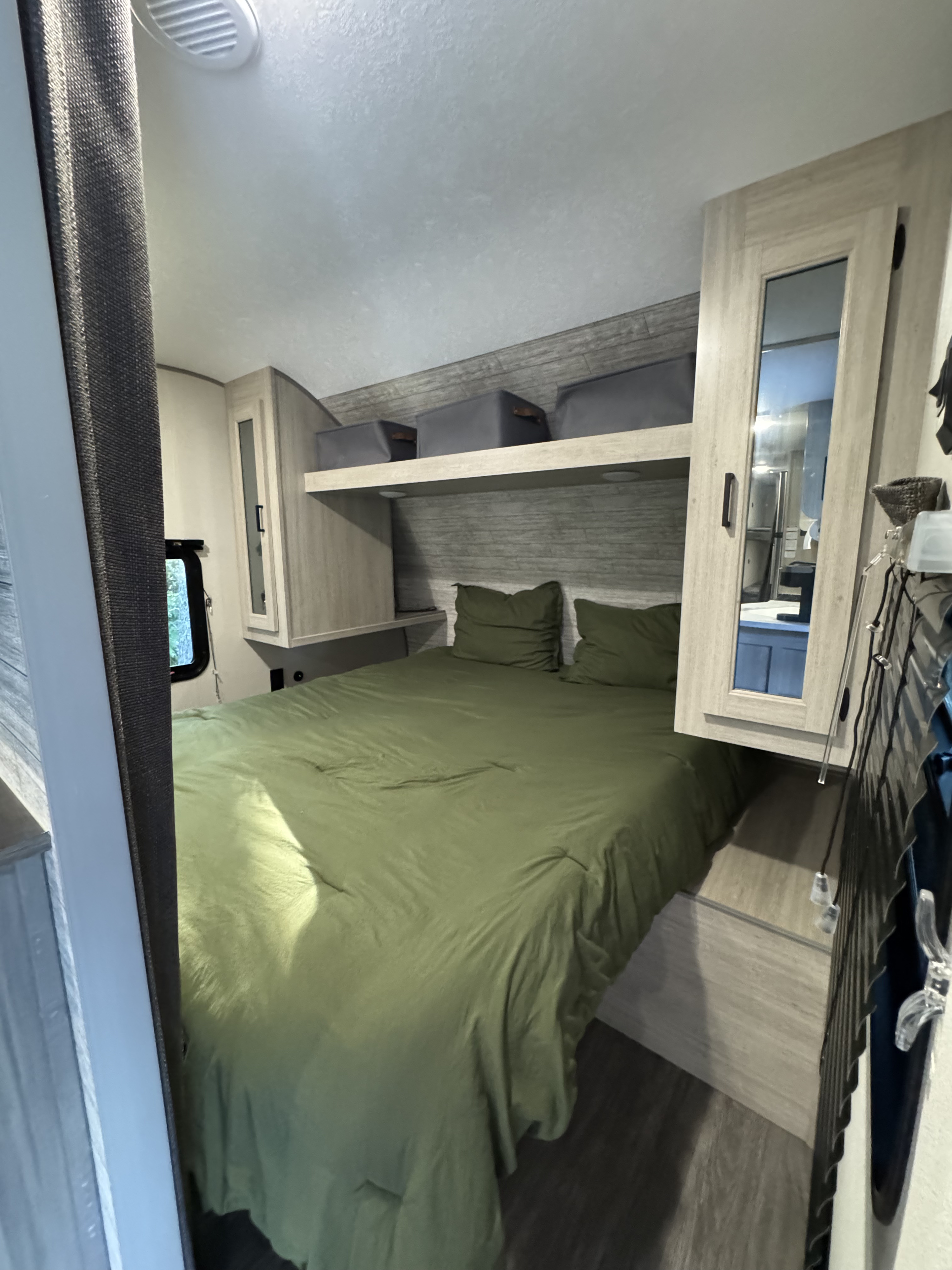 Explore a modern RV rental bedroom featuring a comfy olive green bed, ample overhead storage, and stylish cabinetry.. Forest River Aurora Light 2025