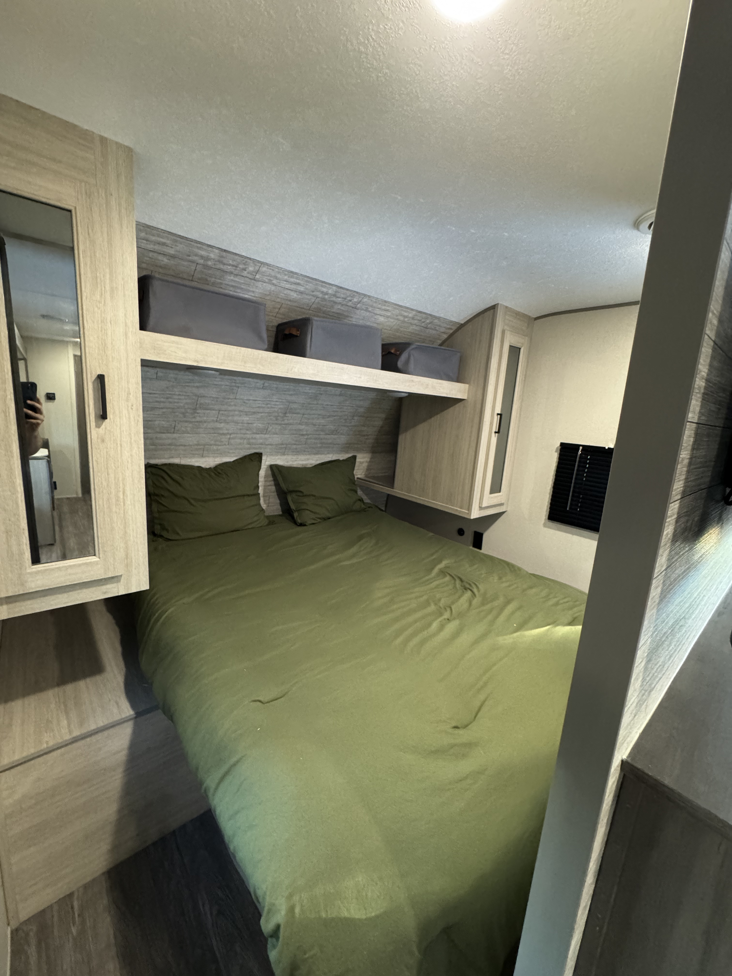 An inviting RV rental bedroom with a comfortable green bed, overhead storage, and a mirrored cabinet.. Forest River Aurora Light 2025