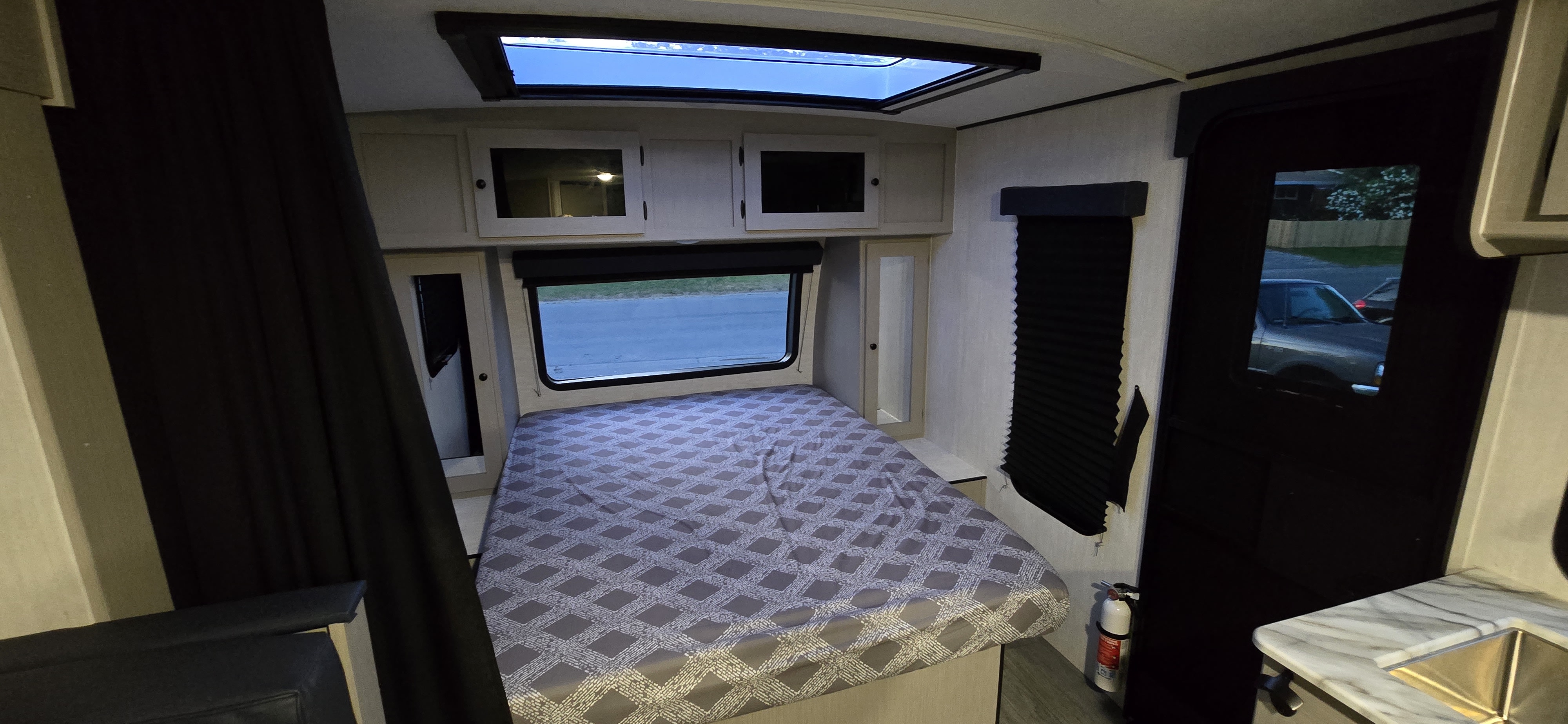 Spacious RV rental bedroom showcasing a comfortable bed, overhead skylight, large window, and visible fire extinguisher.. Coachmen Apex 2025