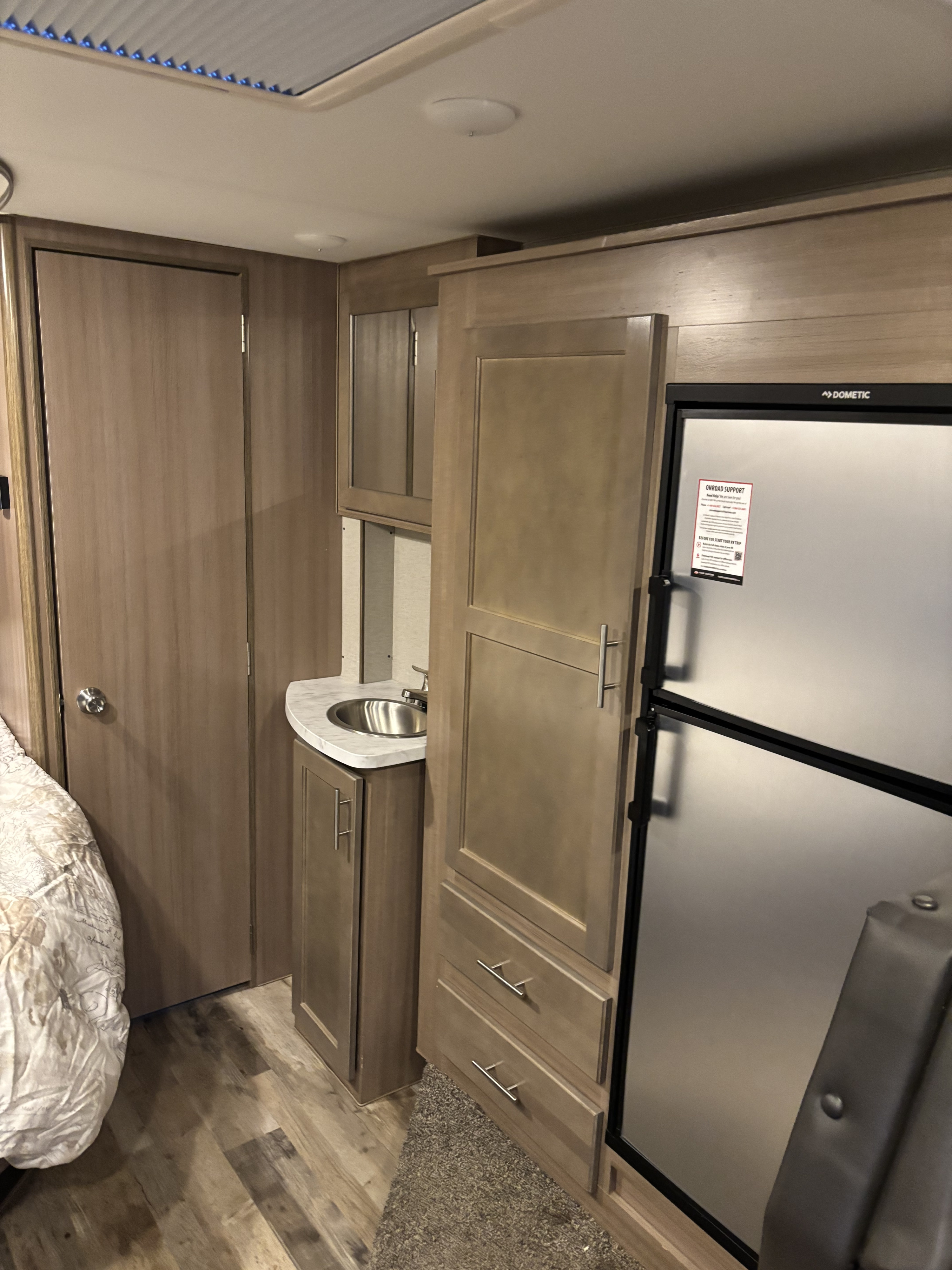 Compact RV rental interior with a cozy bed, kitchenette sink, refrigerator, and wooden cabinetry storage.. Winnebago Adventurer 2021