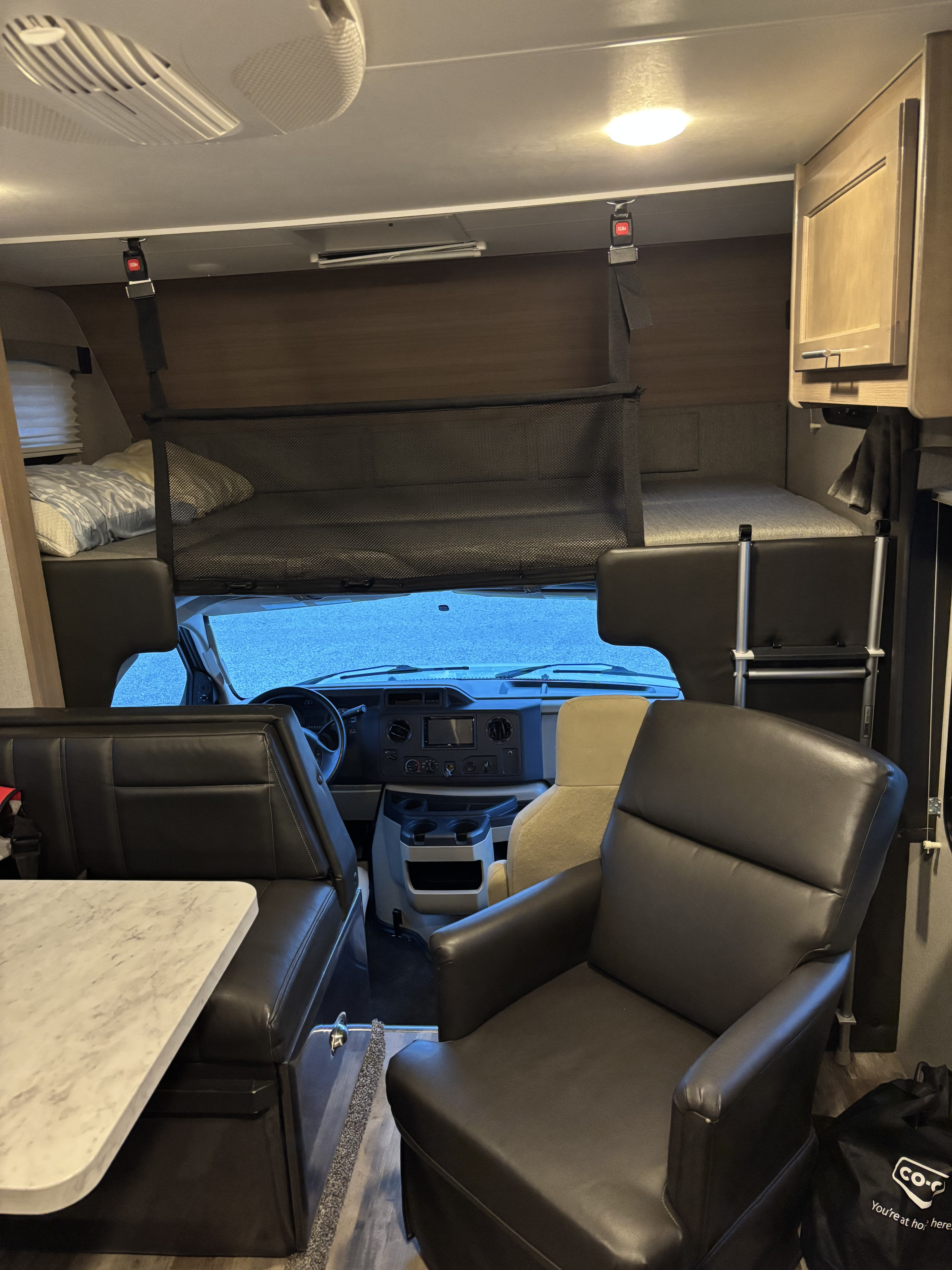 RV rental interior: living area with dinette, comfy chair, driver's cab, and an overhead bunk with safety net.. Winnebago Adventurer 2021