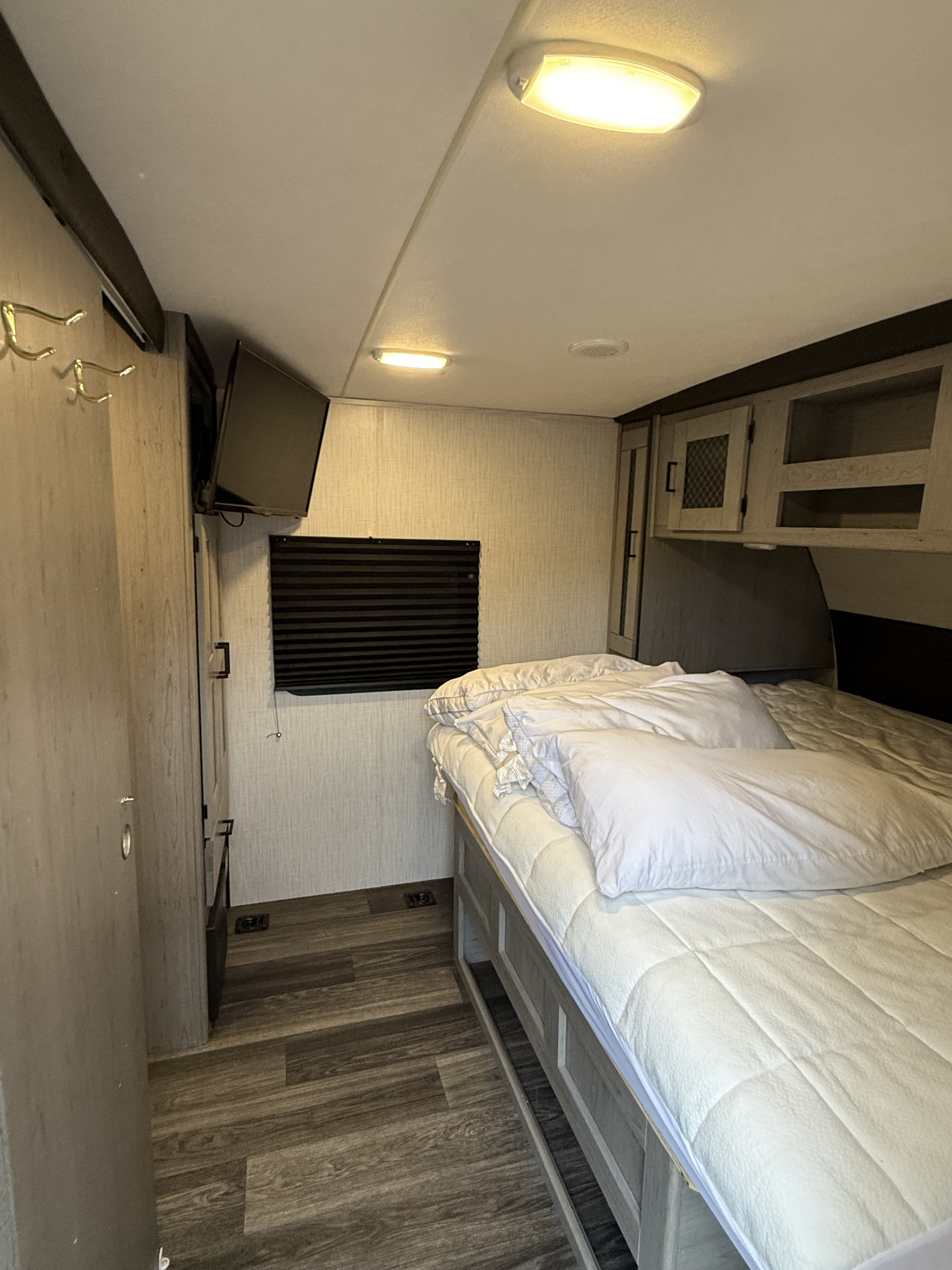 Cozy RV rental bedroom featuring a bed with white bedding, overhead cabinets, a mounted TV, and wood laminate flooring.. Heartland RVs Mallard 2021