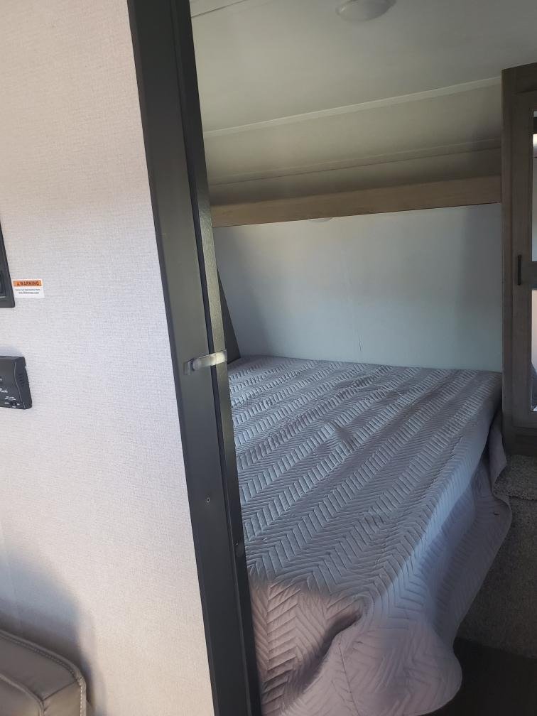 Inside an RV rental: a comfy bedroom featuring a quilted bed and overhead light. Ideal for your next road trip.. Keystone RV Hideout 2021