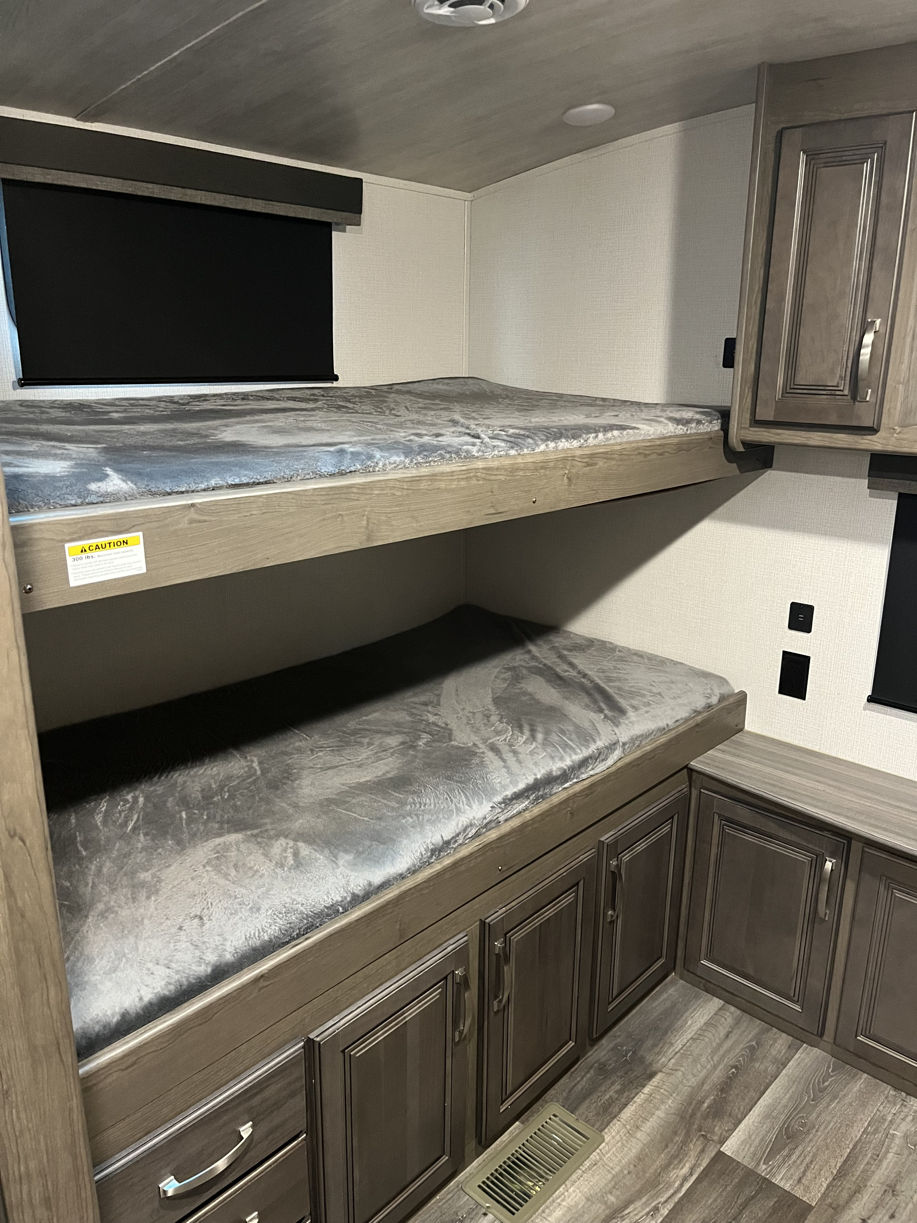 Cozy RV rental bunk beds, perfect for family travel. Features grey mattresses, wood trim, and storage cabinets.. Keystone RV Cougar 2022