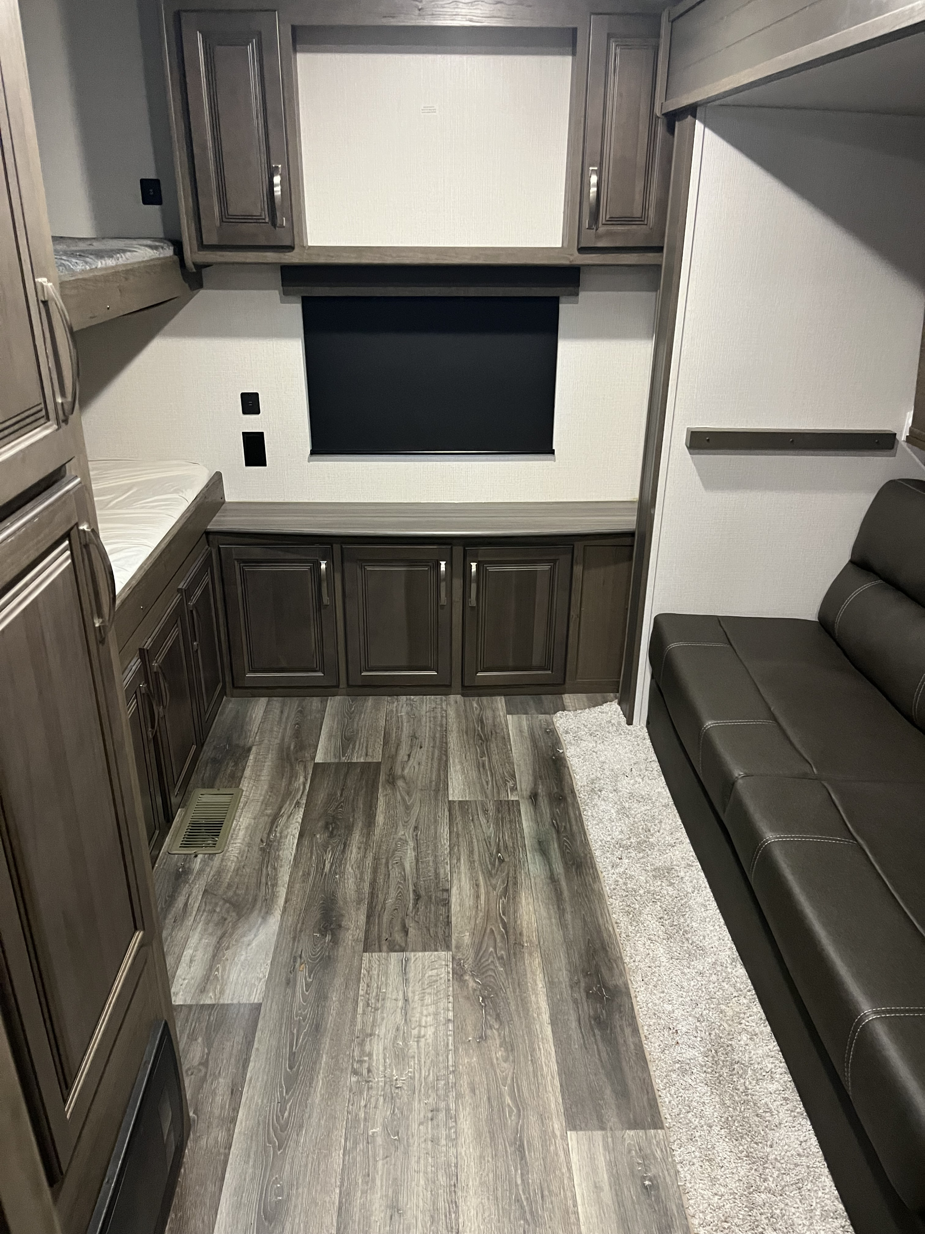 View inside an RV rental showing bunk beds, a dark leather sofa, and wood-tone cabinets/flooring.. Keystone RV Cougar 2022
