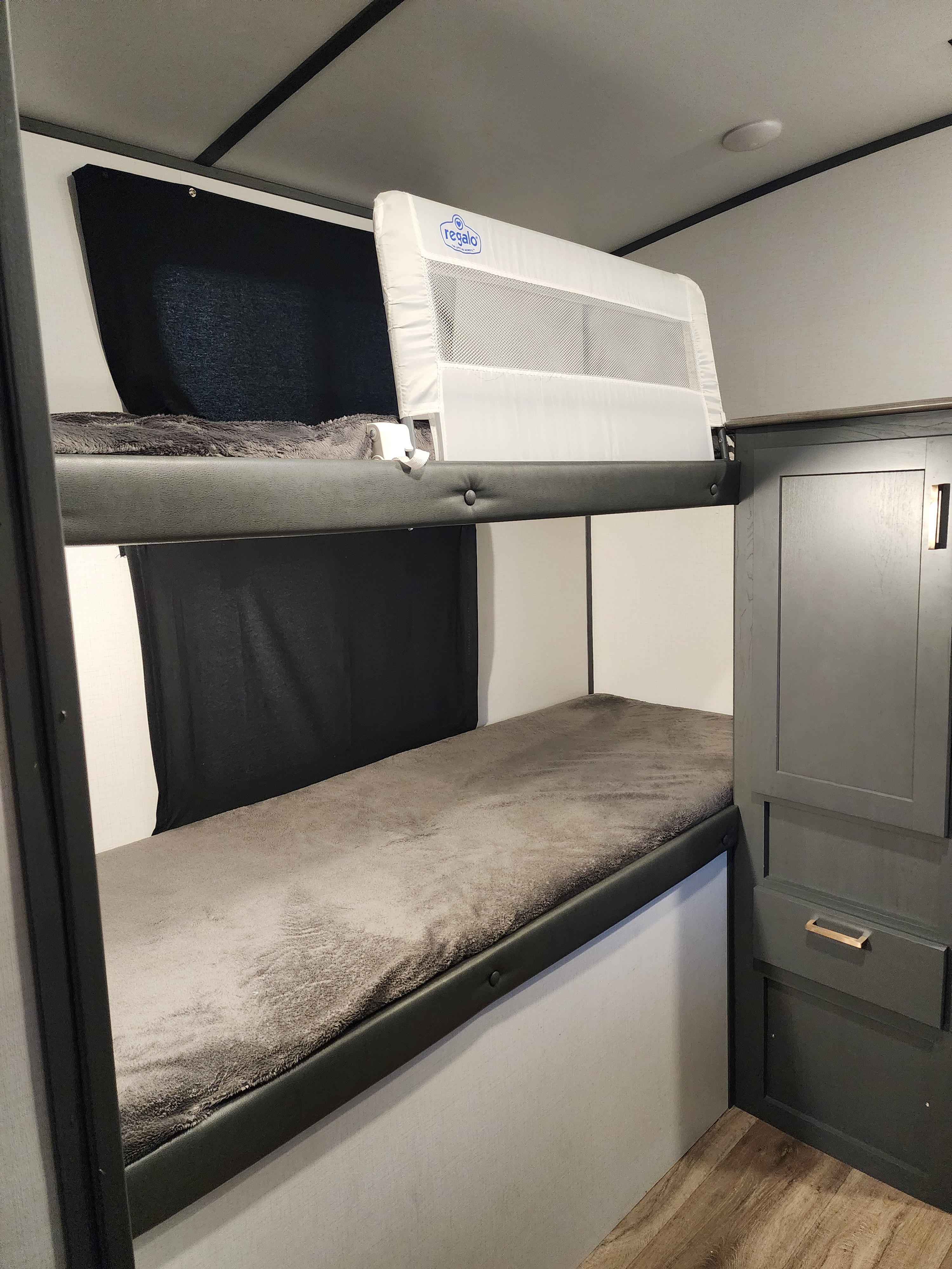 This RV rental features stacked bunk beds with soft gray blankets, dark privacy shades, and a child safety rail on the top bunk.. Keystone RV Bullet Ultra Lite 2023