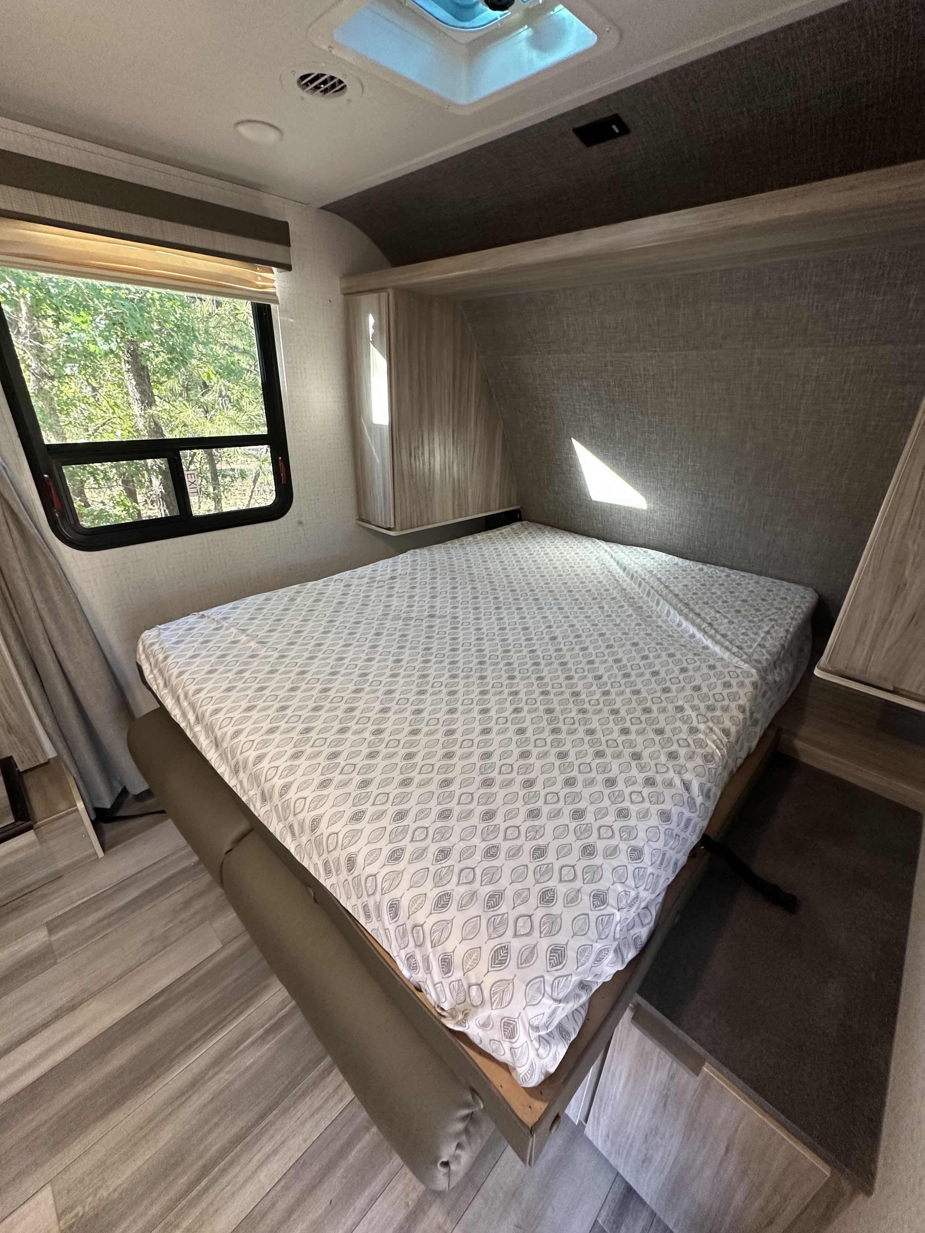 Inside an RV rental: a cozy bedroom featuring a comfortable bed with a leaf pattern, large window, and overhead storage.. Winnebago Minnie Winnie 2021