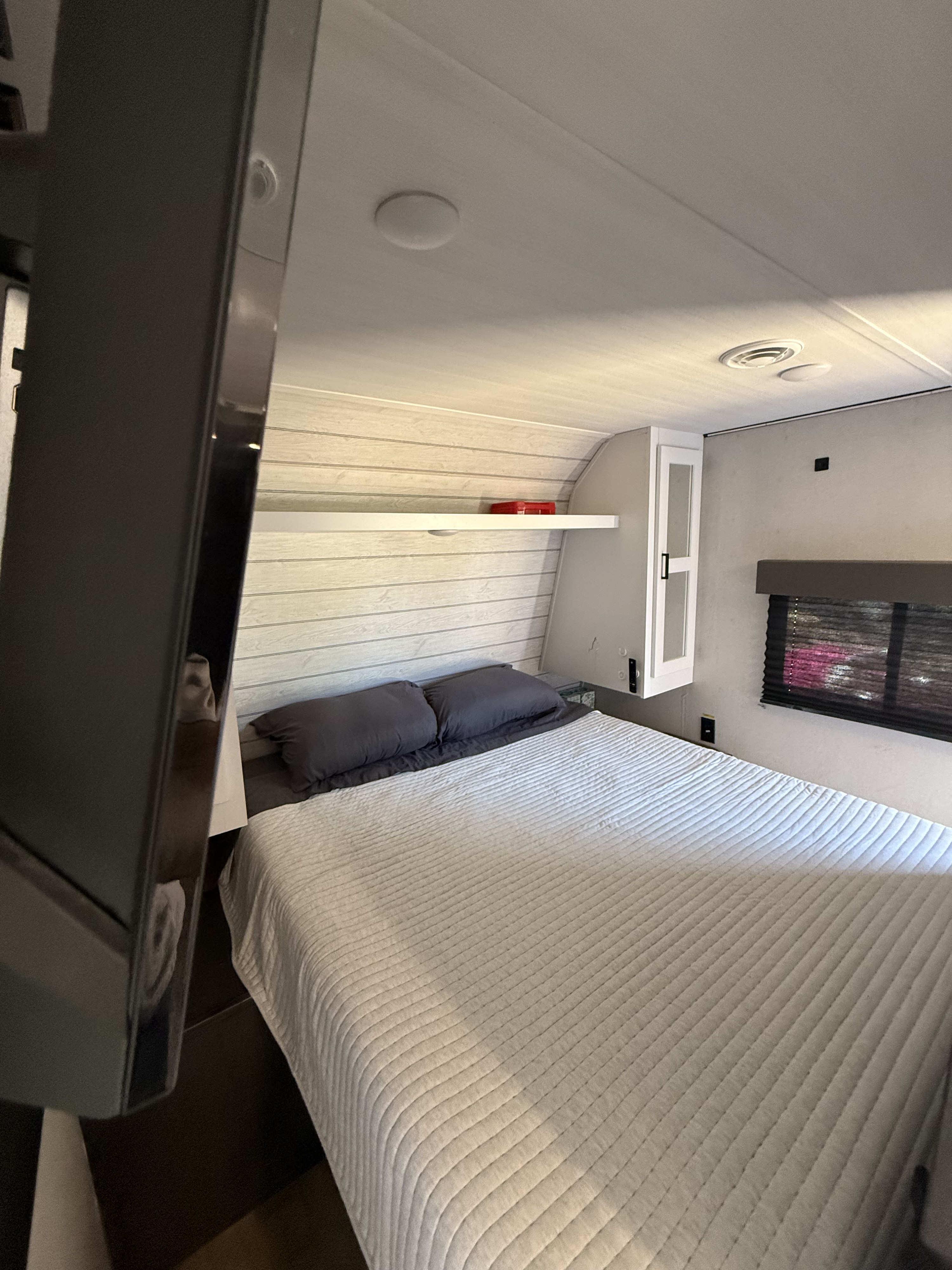 A cozy RV rental bedroom showing a comfortable bed, overhead shelf, window, and mounted TV.. Keystone RV Hideout 2023