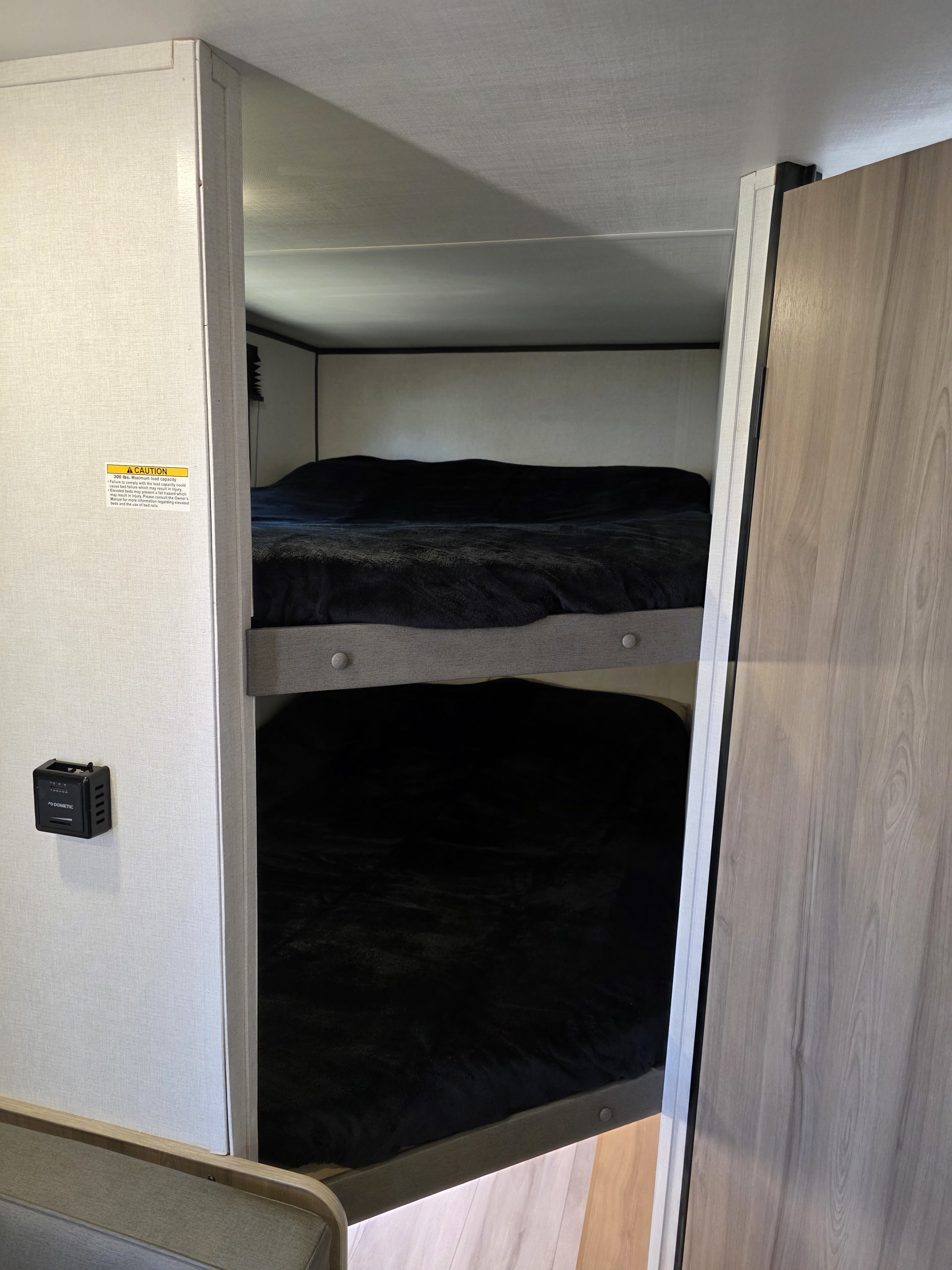 RV rental bunk beds are visible, featuring two cozy bunks with black blankets, a thermostat, and a bed safety warning.. Keystone Coleman 2025
