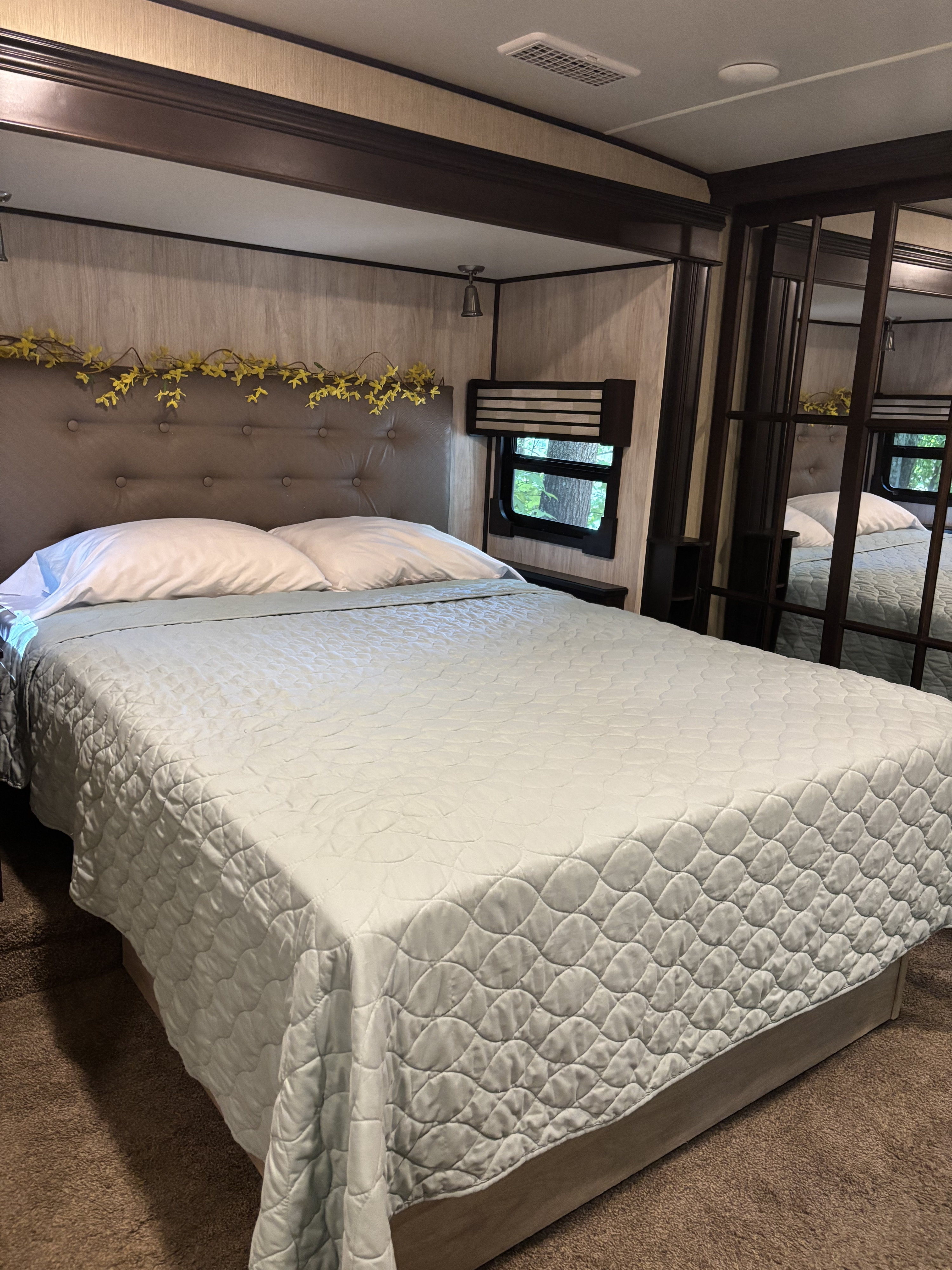 A comfortable RV bedroom, featuring a plush bed, tufted headboard, and nature view from the window. Book your rv rental today!. 4x4fcmp23h6007284 Columbus 2017