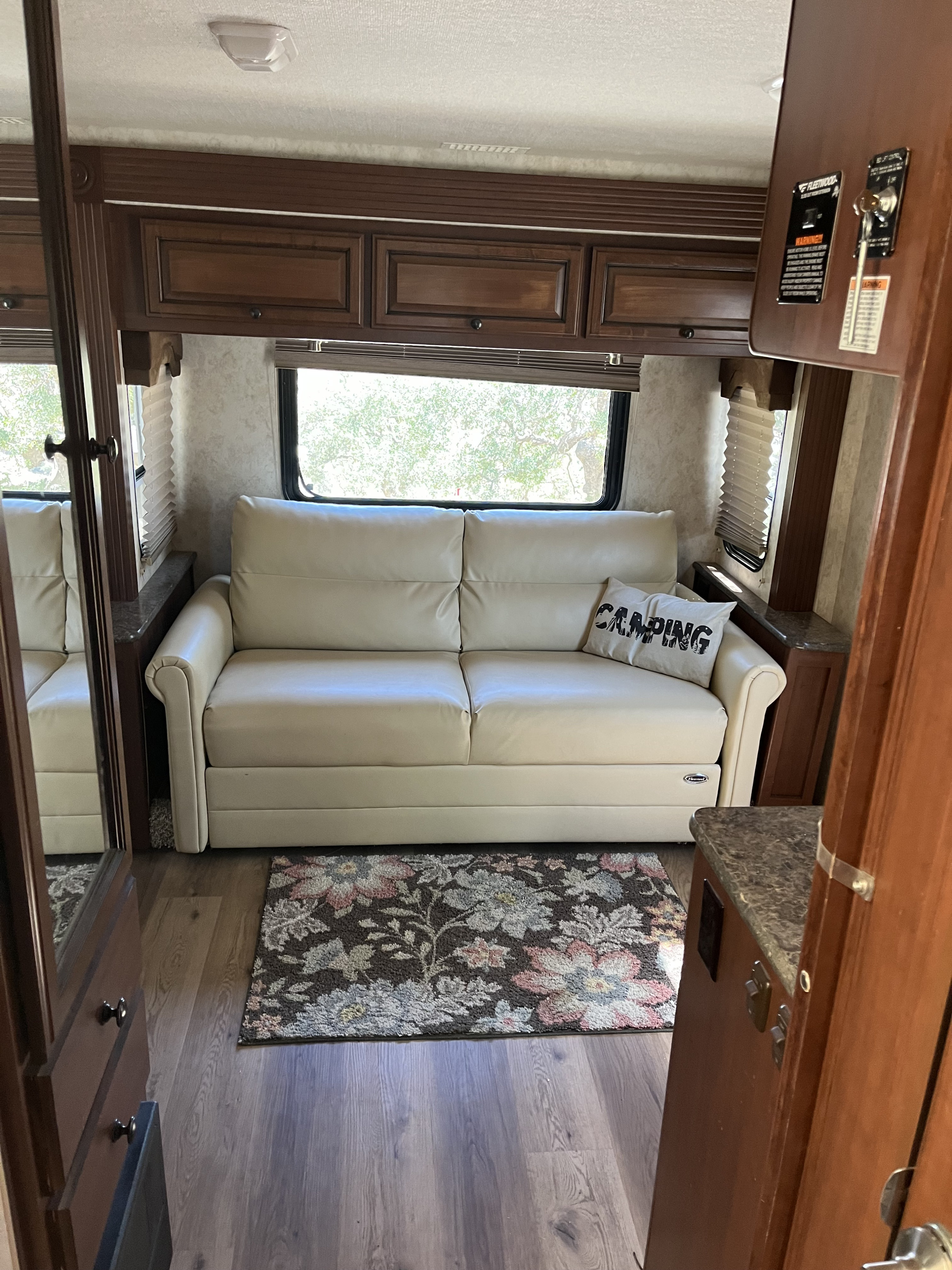 Spacious RV rental interior: cream sofa with "CAMPING" pillow, patterned rug, wood cabinetry, and large windows for light.. Jamboree Sport 2012