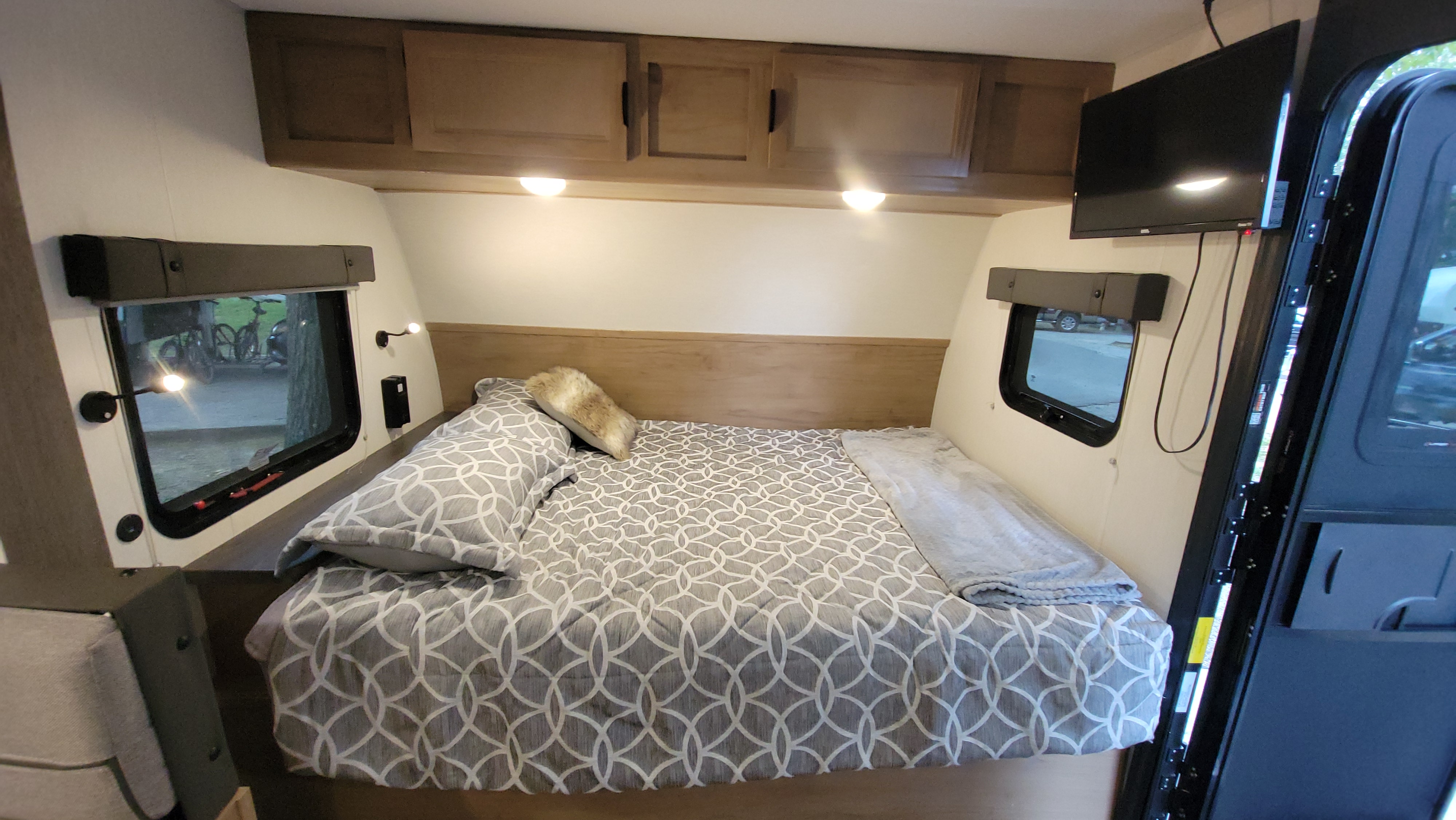 Cozy RV rental bedroom featuring a patterned bed, overhead cabinets, and dual windows. Ideal for comfortable travel.. Forest River Cherokee Wolf Pup 2024