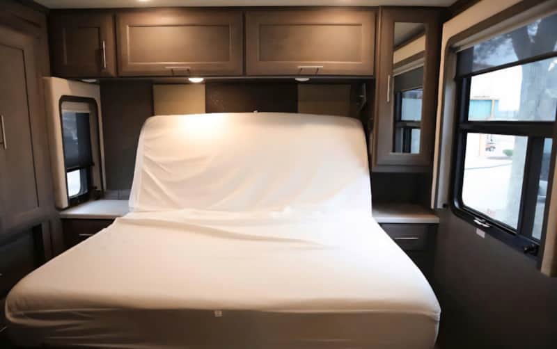 Comfortable RV rental bedroom with a neatly made bed, overhead storage, and natural light from the windows.. Thor Palazzo 2022